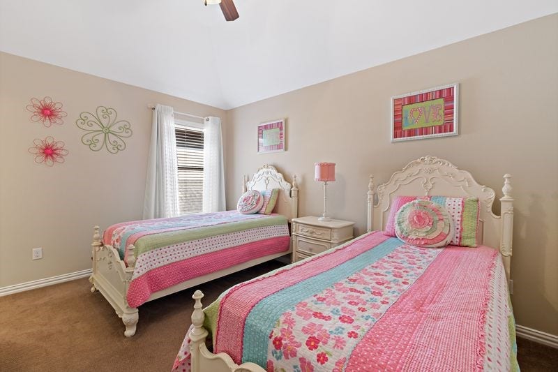 22 Waters Lake Boulevard, Missouri City, TX 77459 Charming bedroom with two twin beds featuring pastel floral bedding, elegant vintage-style headboards, and a cozy atmosphere accentuated by soft wall decor and natural light.