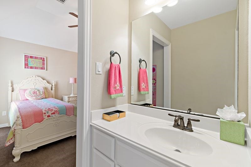22 Waters Lake Boulevard, Missouri City, TX 77459 Charming bedroom with pastel decor and an adjoining bathroom featuring a sleek vanity and ample lighting.