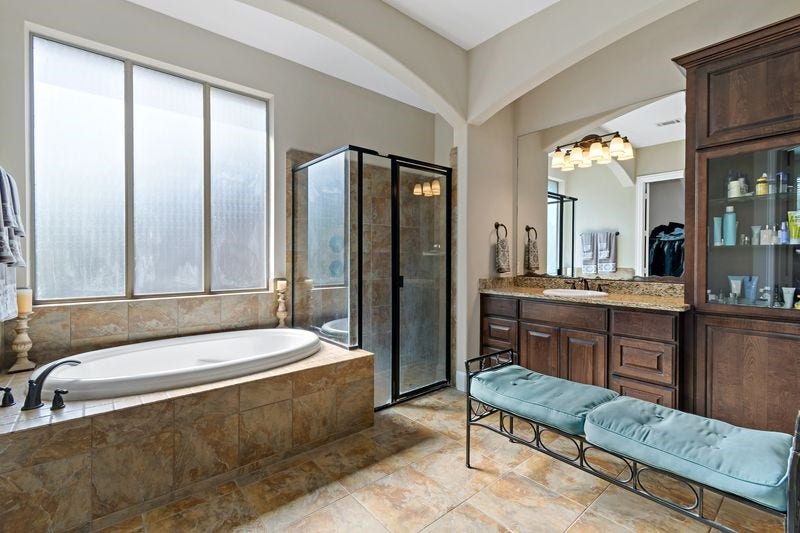 22 Waters Lake Boulevard, Missouri City, TX 77459 Spacious bathroom featuring a luxurious soaking tub, a separate glass-enclosed shower, and a dual-sink vanity with rich wood cabinetry, all accented by elegant tile flooring and abundant natural light.