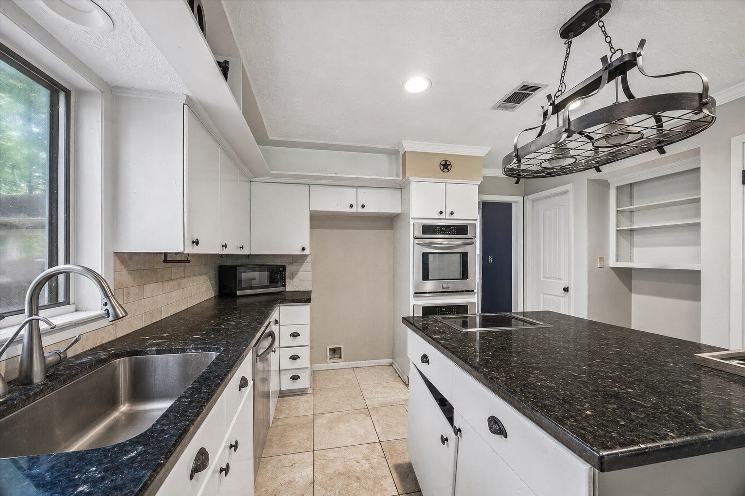 226 S Pine Drive, Montgomery, TX 77356 Dark granite counters anchor a kitchen with white cabinetry, a central island, and double wall ovens. An oversized window above the sink brings leafy views into daily meal preparation.
