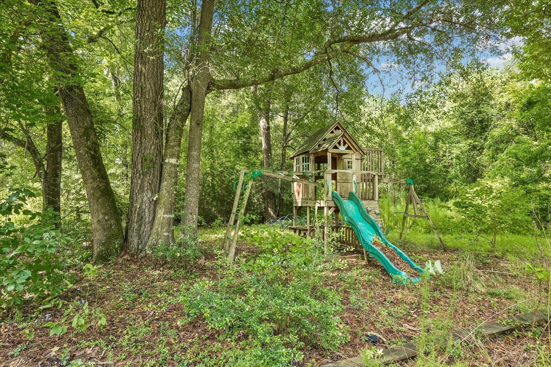 226 S Pine Drive, Montgomery, TX 77356 A raised wooden play structure with a green slide nestles among mature trees. The shaded setting creates a tucked-away corner for outdoor play.