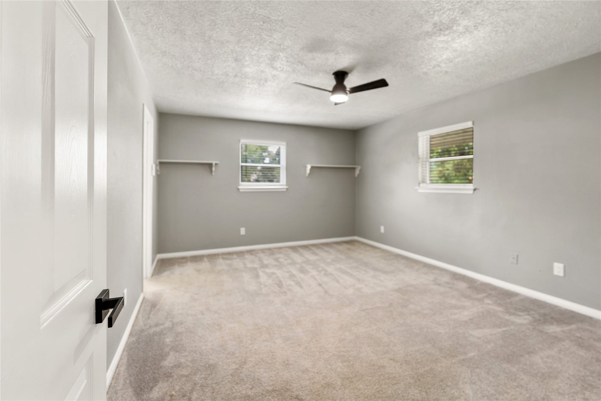 207 Burgundy Lane, League City, TX 77573 One of two spacious secondary bedrooms with carpeted flooring, featuring two windows that provide natural light. It has a modern ceiling fan and wall-mounted shelves, offering a versatile space for personalization.