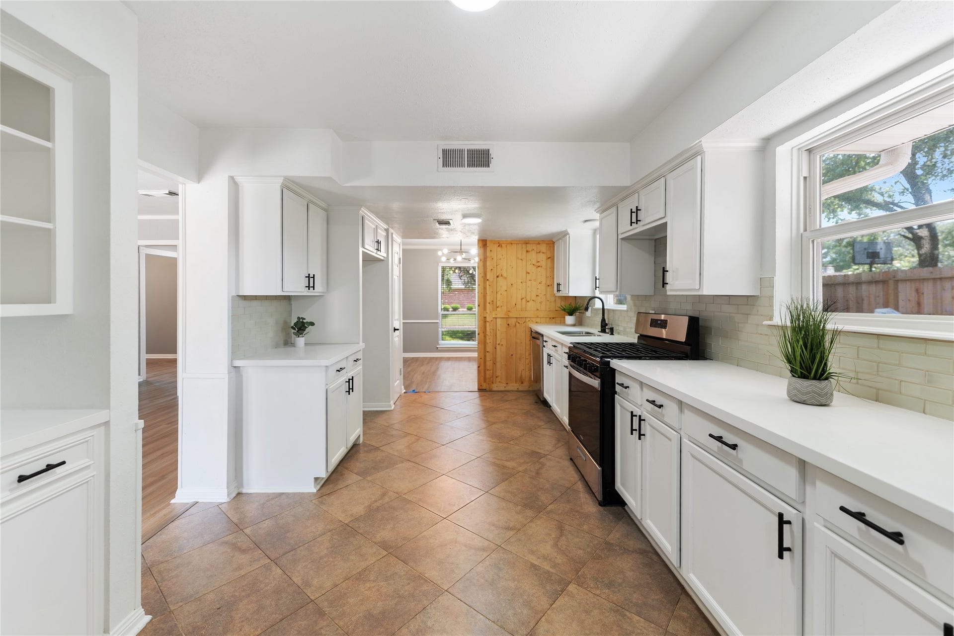 207 Burgundy Lane, League City, TX 77573 The kitchen features a modern, spacious design with white cabinetry and contrasting black hardware. It has ample counter space, gas stove, and large windows for natural light, creating an inviting cooking environment.