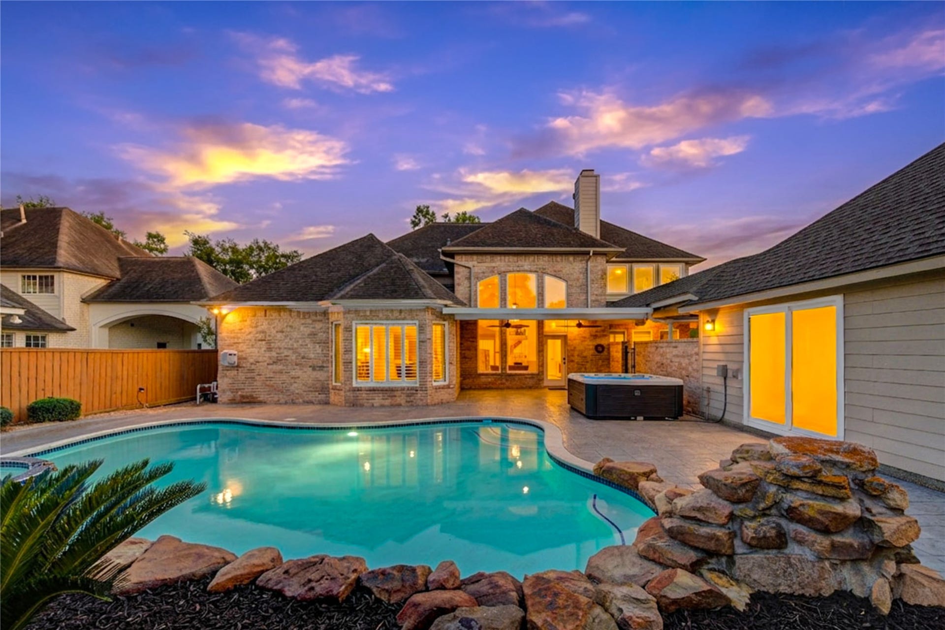 12806 Rock Falls Way, Houston, TX 77041 Covered patio with ceiling fan overlooks a sparkling pool, offering a perfect outdoor living space for relaxation and entertaining, set against a stunning two-story brick home.