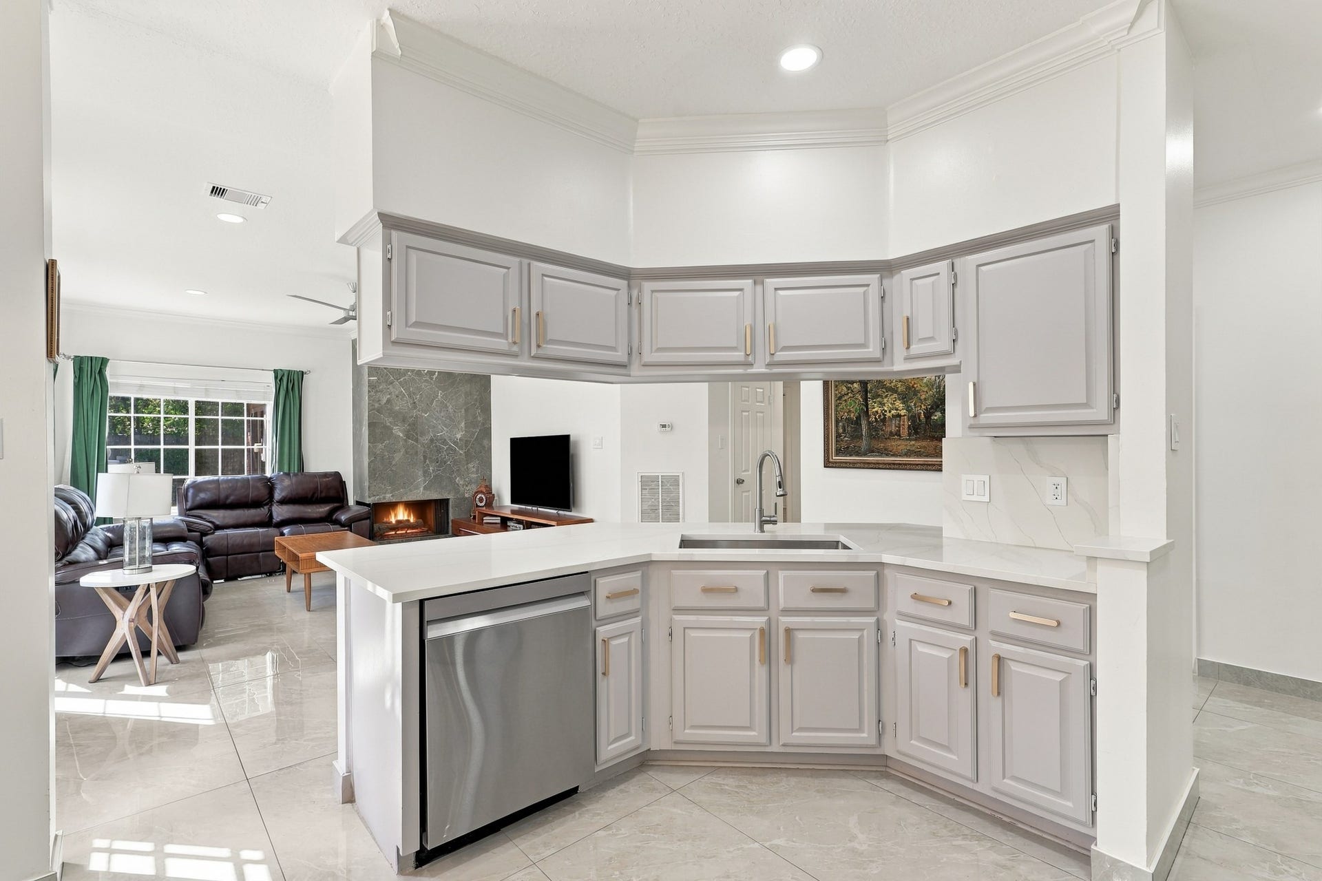 14538 Circlewood Way, Houston, TX 77062 Thoughtfully designed kitchen features a wraparound breakfast bar with generous counter space, abundant gray cabinetry accented by brushed gold hardware, and a stainless steel dishwasher. The open pass-through maintains a connection to the living area, while crown molding, recessed lighting, and polished flooring complete the space.