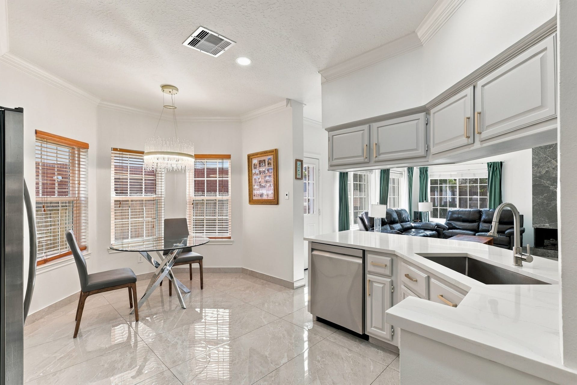 14538 Circlewood Way, Houston, TX 77062 The kitchen opens effortlessly to a sunlit breakfast nook surrounded by windows, creating a welcoming space for casual dining. A convenient pass-through overlooks the living room, while white countertops, gray cabinetry with gold hardware, stainless steel dishwasher, and polished flooring tie the spaces together beautifully.
