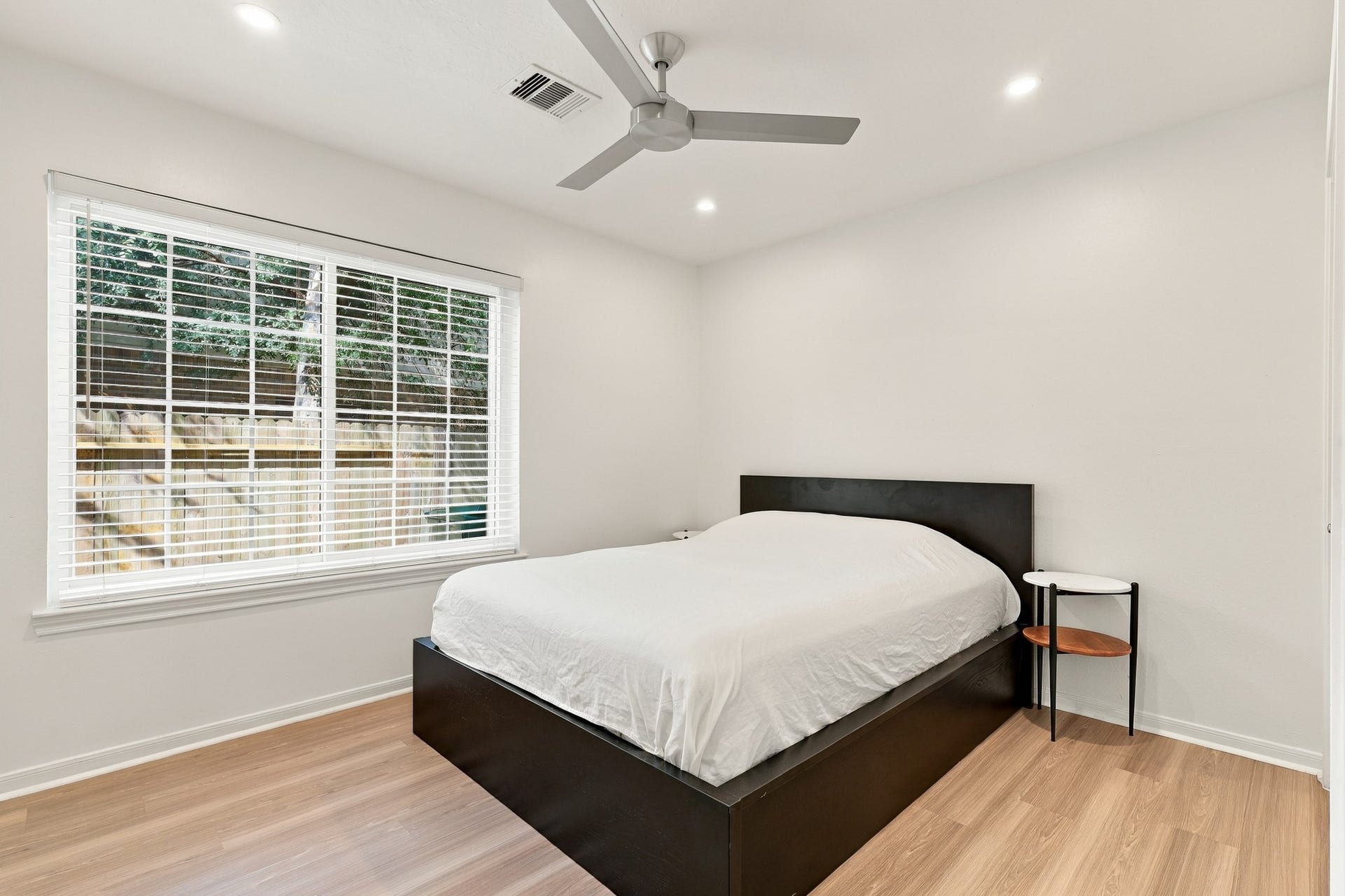 14538 Circlewood Way, Houston, TX 77062 Spacious bedroom featuring warm wood flooring, a large window overlooking the backyard, recessed lighting, and a modern ceiling fan. Crisp white walls and abundant natural light create a bright, inviting retreat.