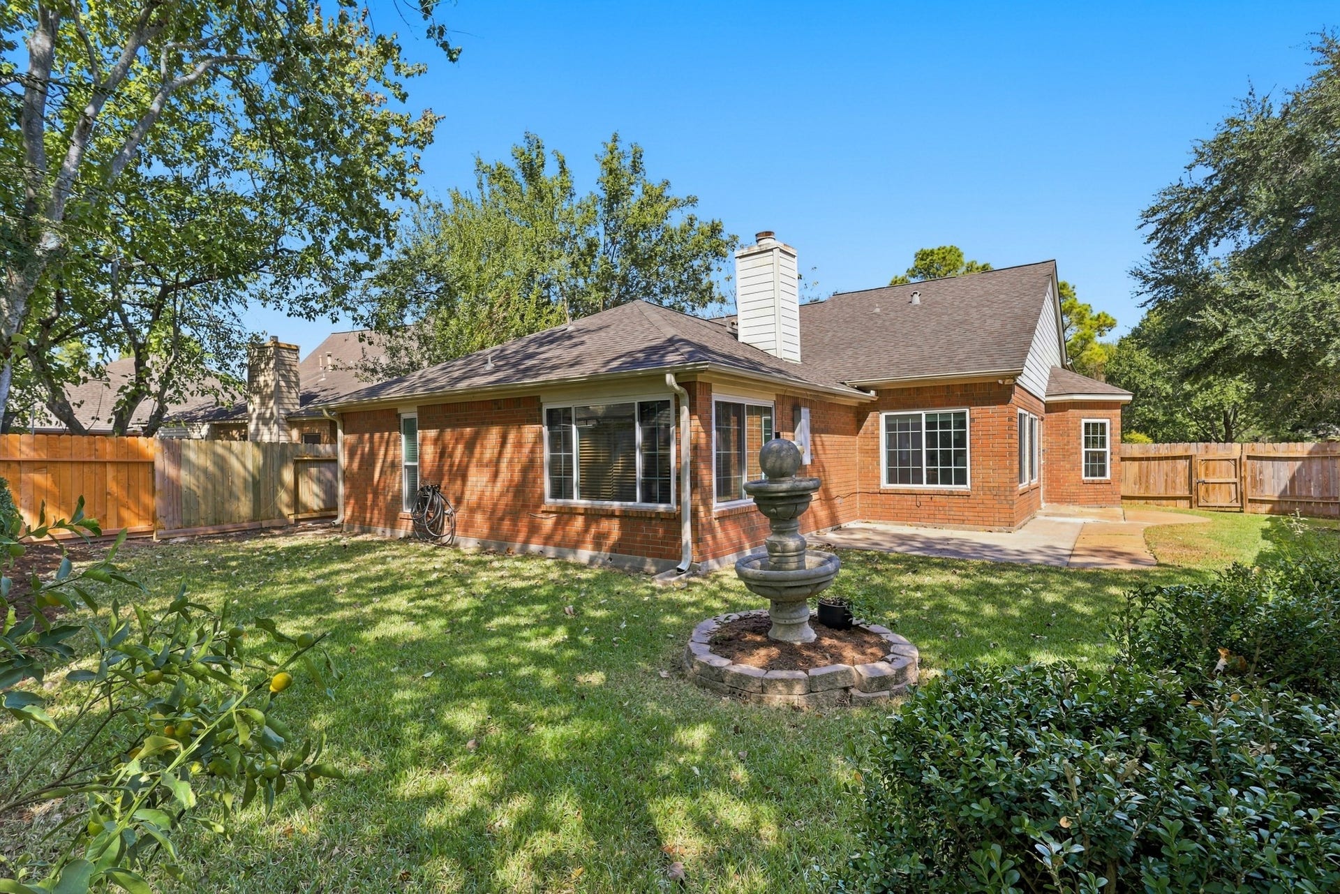 14538 Circlewood Way, Houston, TX 77062 The spacious backyard features a classic brick exterior, mature shade trees, lush greenery, and a fully fenced lawn. A decorative tiered fountain creates a charming focal point, while the generous concrete patio provides an ideal space for outdoor dining, entertaining, or relaxing. Large windows overlook the backyard, bringing natural light into the home and connecting the indoor and outdoor living spaces.