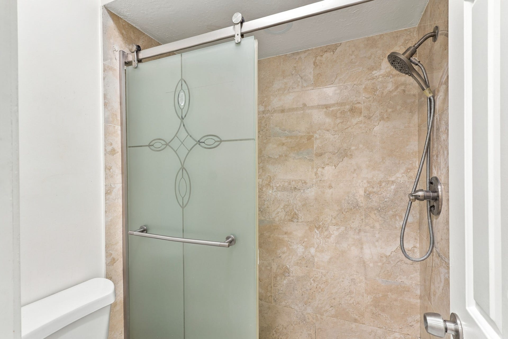14538 Circlewood Way, Houston, TX 77062 Spacious walk-in shower featuring neutral stone tile extending to the ceiling, a decorative frosted glass sliding door with brushed nickel hardware, and a convenient handheld showerhead.