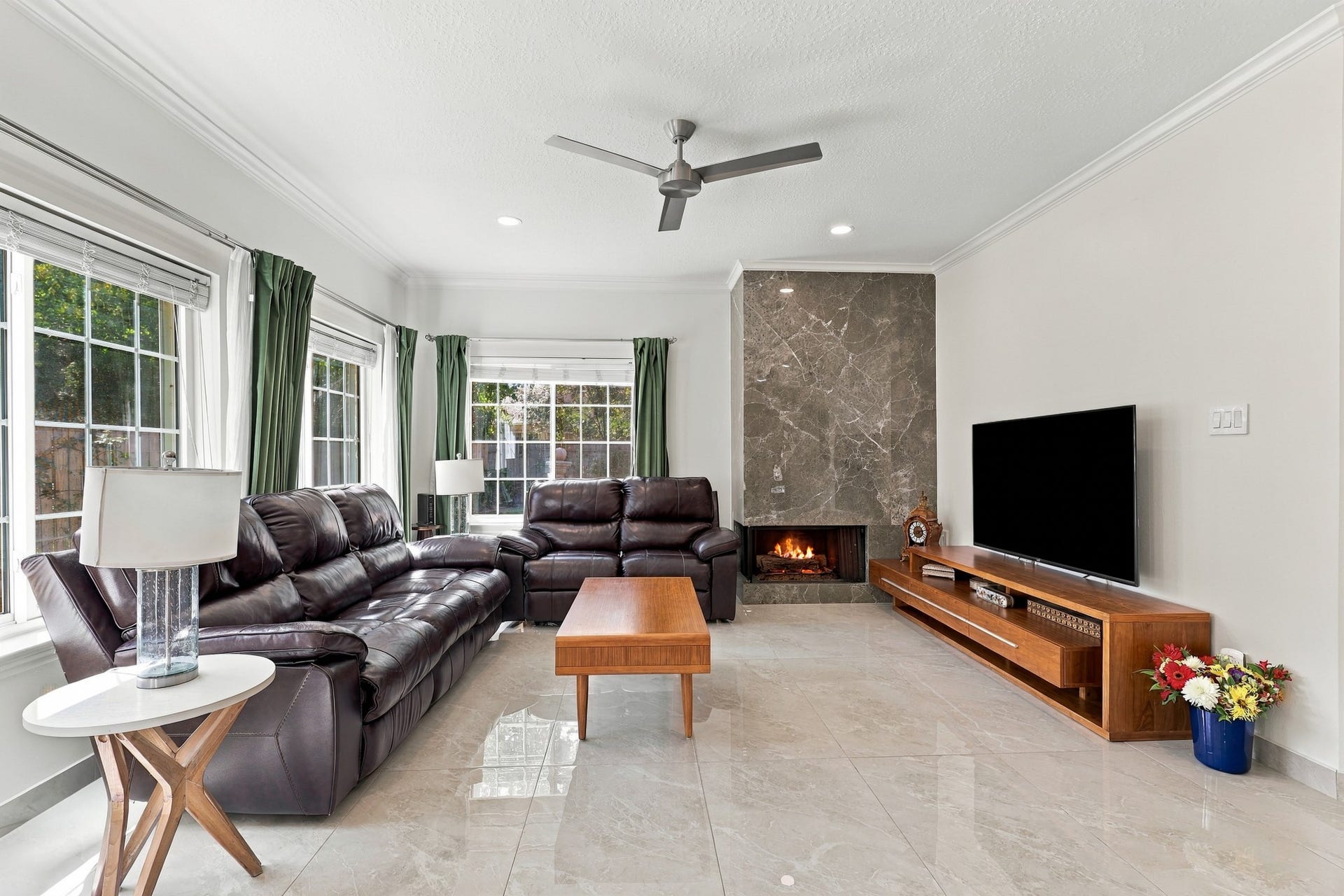14538 Circlewood Way, Houston, TX 77062 Another view of the inviting living room showcases the generous seating area, abundant natural light, and beautiful marble tile flooring. A floor-to-ceiling fireplace with dramatic surround anchors the space, complemented by crown molding, recessed lighting, and a sleek contemporary ceiling fan.