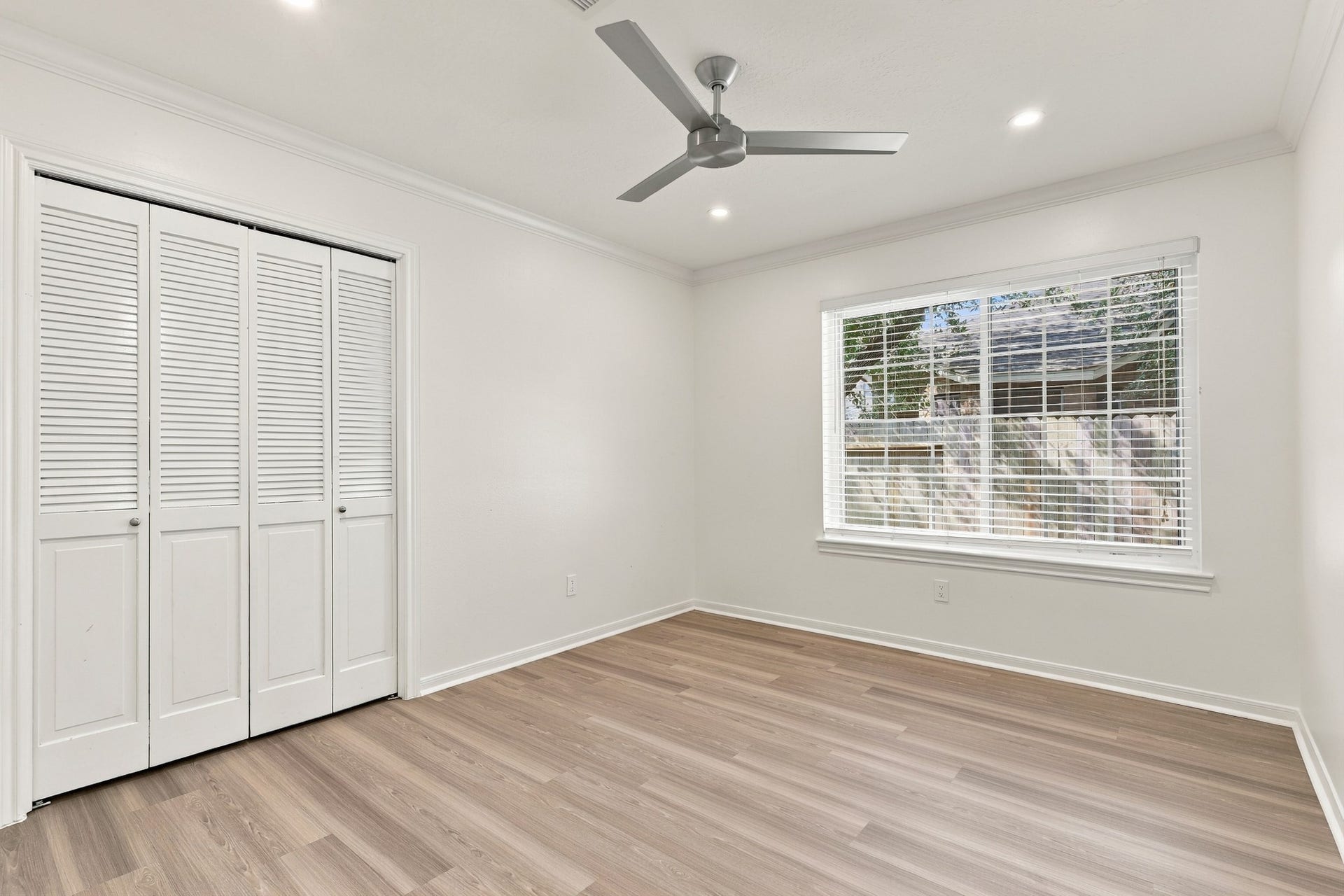 14538 Circlewood Way, Houston, TX 77062 Bright, spacious bedroom featuring wood flooring, crown molding, recessed lighting, and a modern ceiling fan. A large window provides natural light, while a generous double closet with louvered doors offers ample storage.