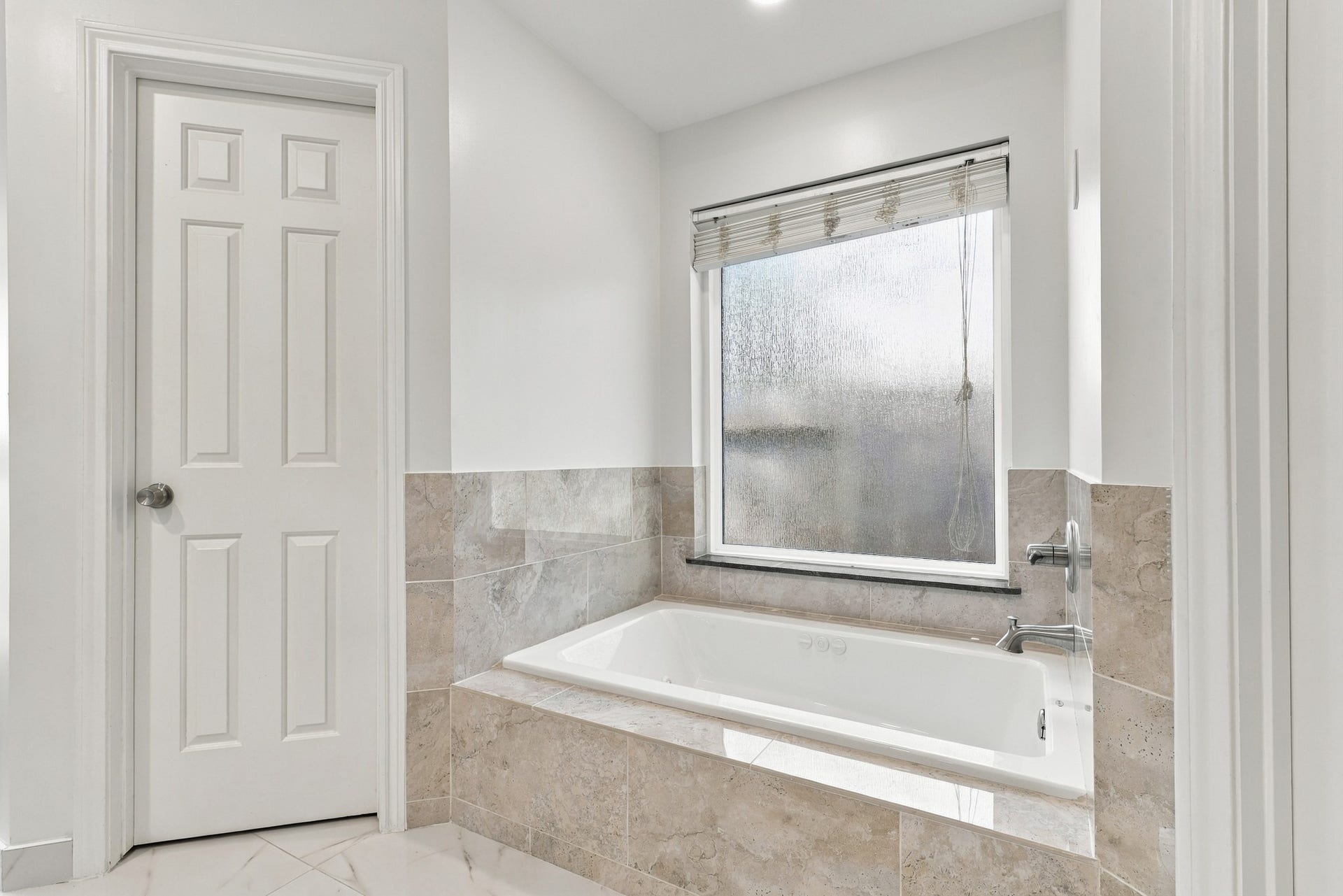 14538 Circlewood Way, Houston, TX 77062 Primary bathroom features a relaxing jetted soaking tub surrounded by neutral stone tile, with a large frosted window providing natural light and privacy. A perfect spot to unwind at the end of the day.