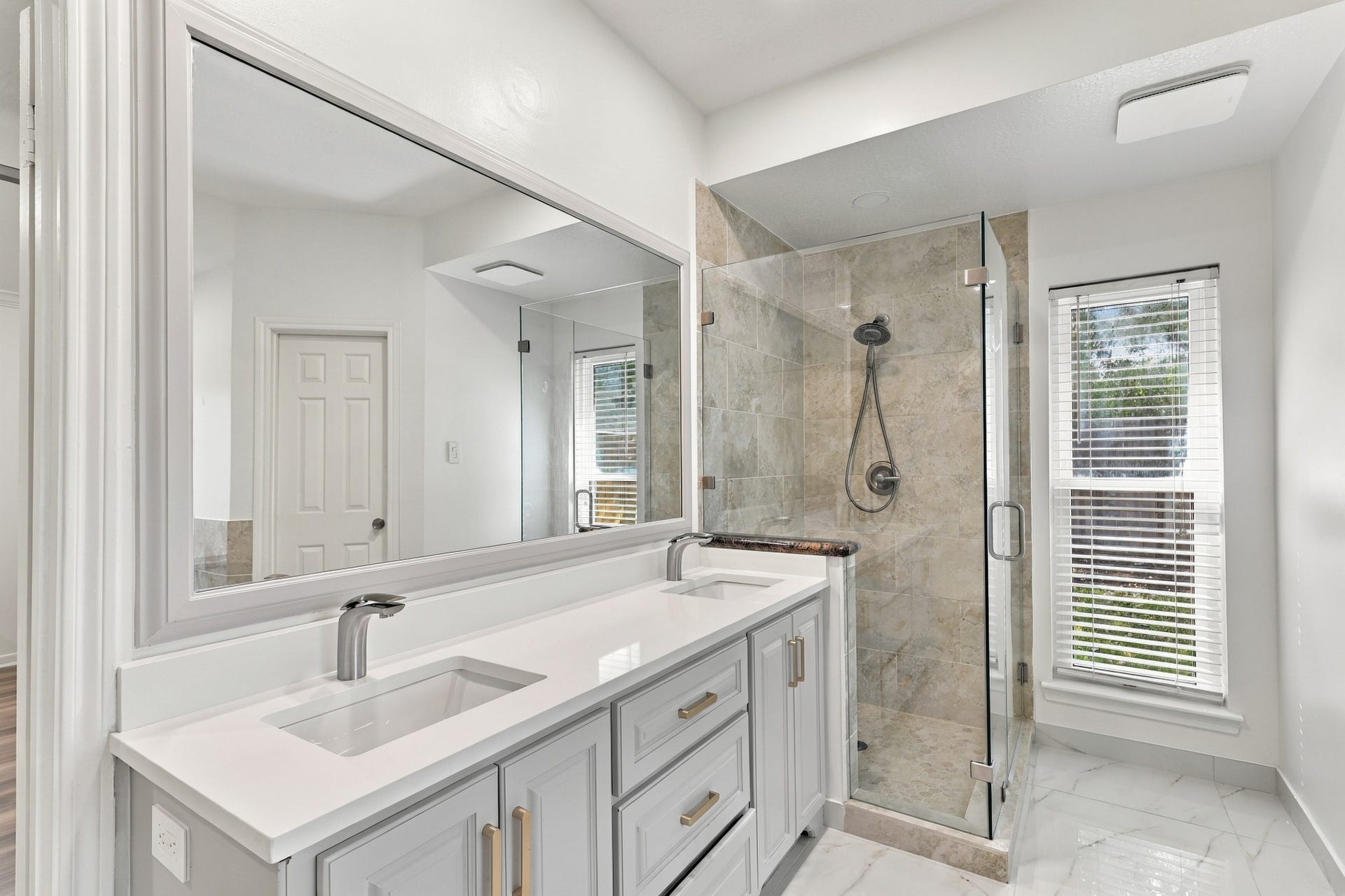 14538 Circlewood Way, Houston, TX 77062 The primary bathroom features a spacious double-sink vanity with sleek countertops, gray cabinetry, gold-toned hardware, and an oversized mirror. A separate glass-enclosed walk-in shower with neutral stone tile completes the bright, modern space.