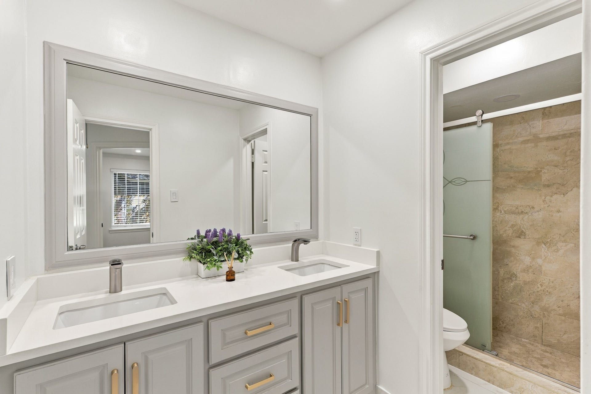 14538 Circlewood Way, Houston, TX 77062 Beautifully updated bathroom featuring a spacious double-sink vanity with sleek countertops, gray cabinetry, brushed gold hardware, and a large framed mirror. The adjoining walk-in shower features floor-to-ceiling tile and a frosted glass enclosure.