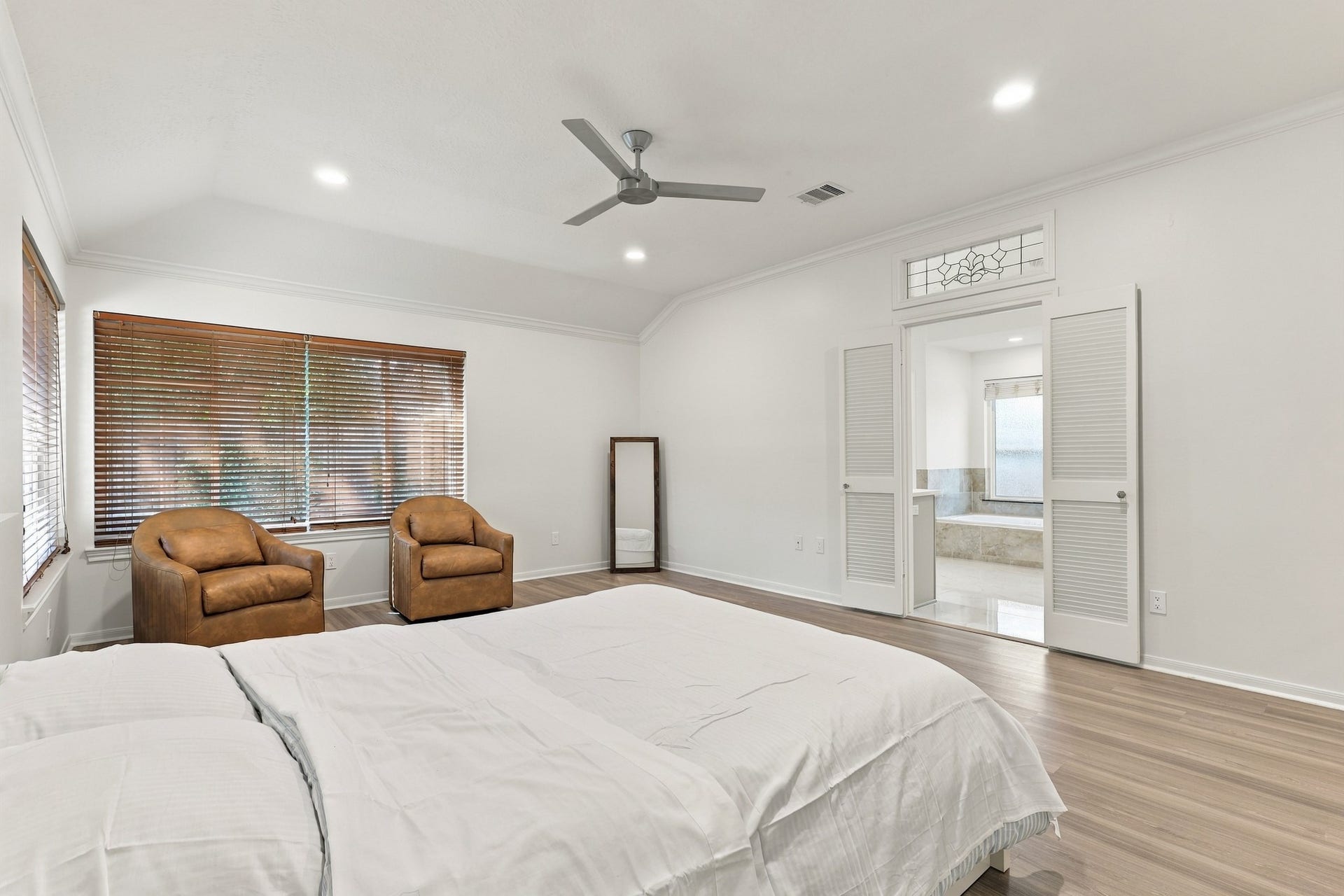 14538 Circlewood Way, Houston, TX 77062 Another view of the spacious primary suite highlights the vaulted ceiling, crown molding, wood flooring, and comfortable sitting area. Decorative glass transom and double louvered doors create an elegant entrance to the adjoining primary bathroom.
