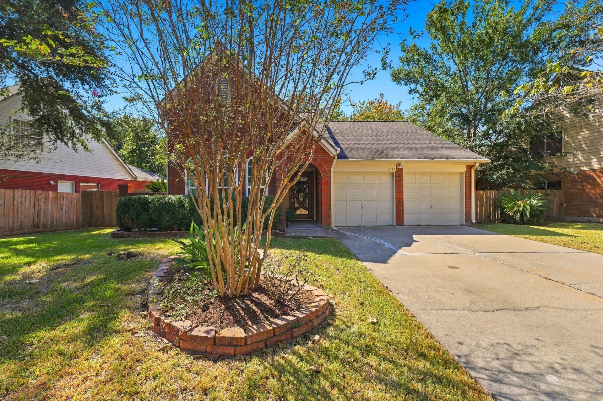 14538 Circlewood Way, Houston, TX 77062 A closer look at the home's inviting curb appeal, featuring a charming arched entry with decorative front door, mature landscaping, brick-bordered planting beds, and a spacious driveway leading to the attached two-car garage.