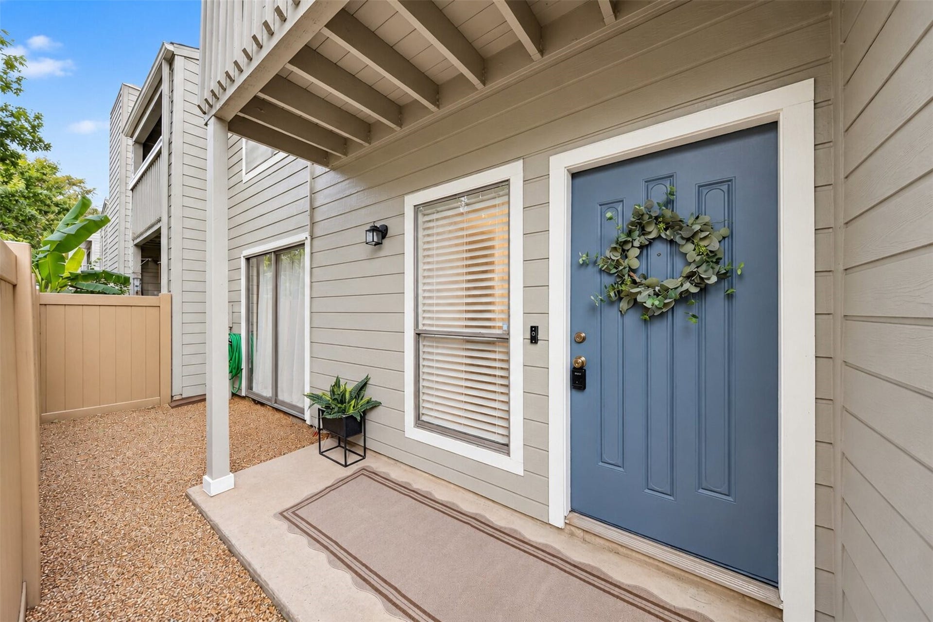 2379 Briarwest Boulevard, #85, Houston, TX 77077 A covered front porch leads to the blue entry door, dressed with a eucalyptus wreath and keypad lock. Beside it, a private fenced side patio with sliding glass door extends the living space outdoors.