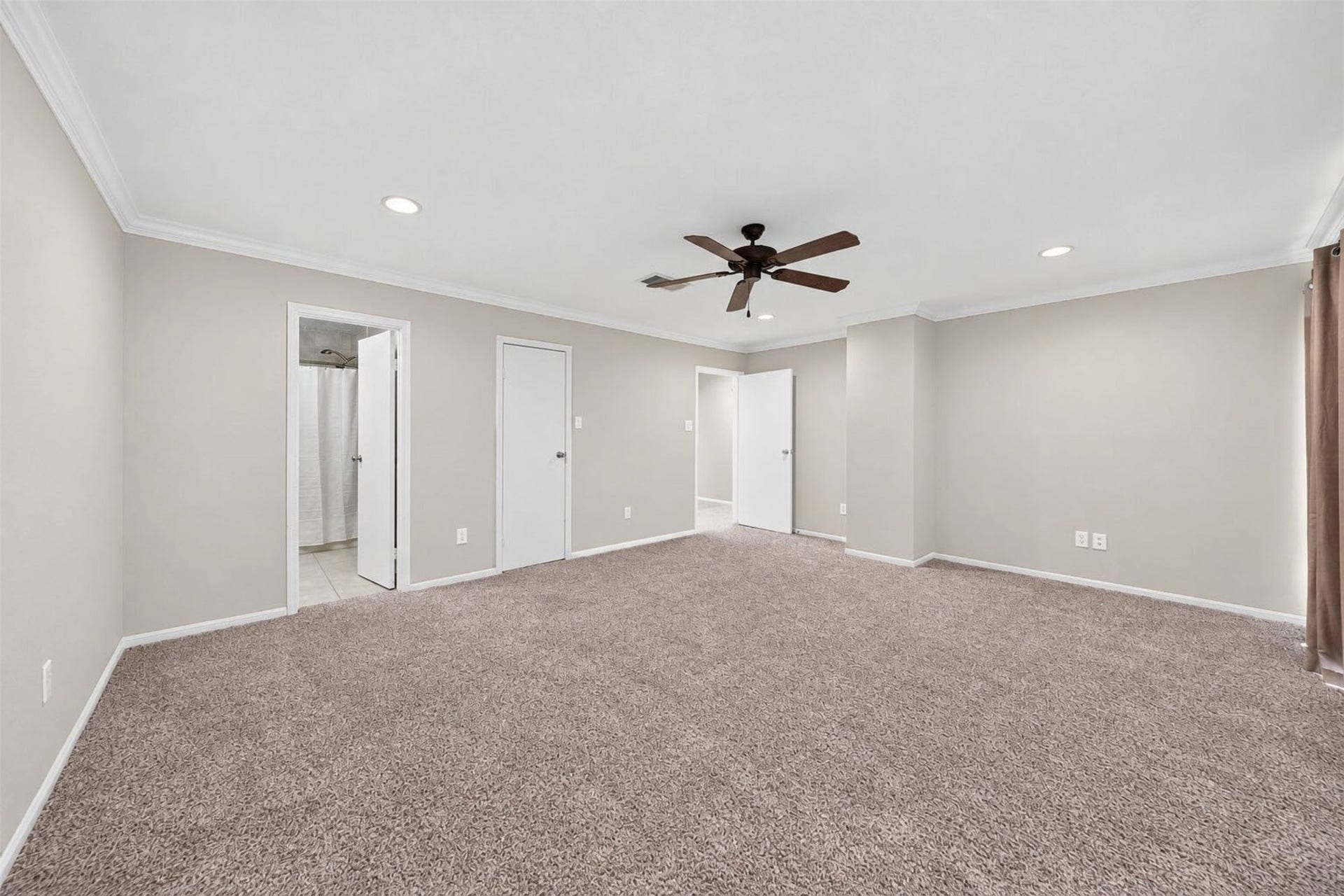 2379 Briarwest Boulevard, #85, Houston, TX 77077 From the window corner, the primary bedroom shows its ensuite bath doorway, a closet door, and the hall entry. Plush carpet and a ceiling fan throughout.