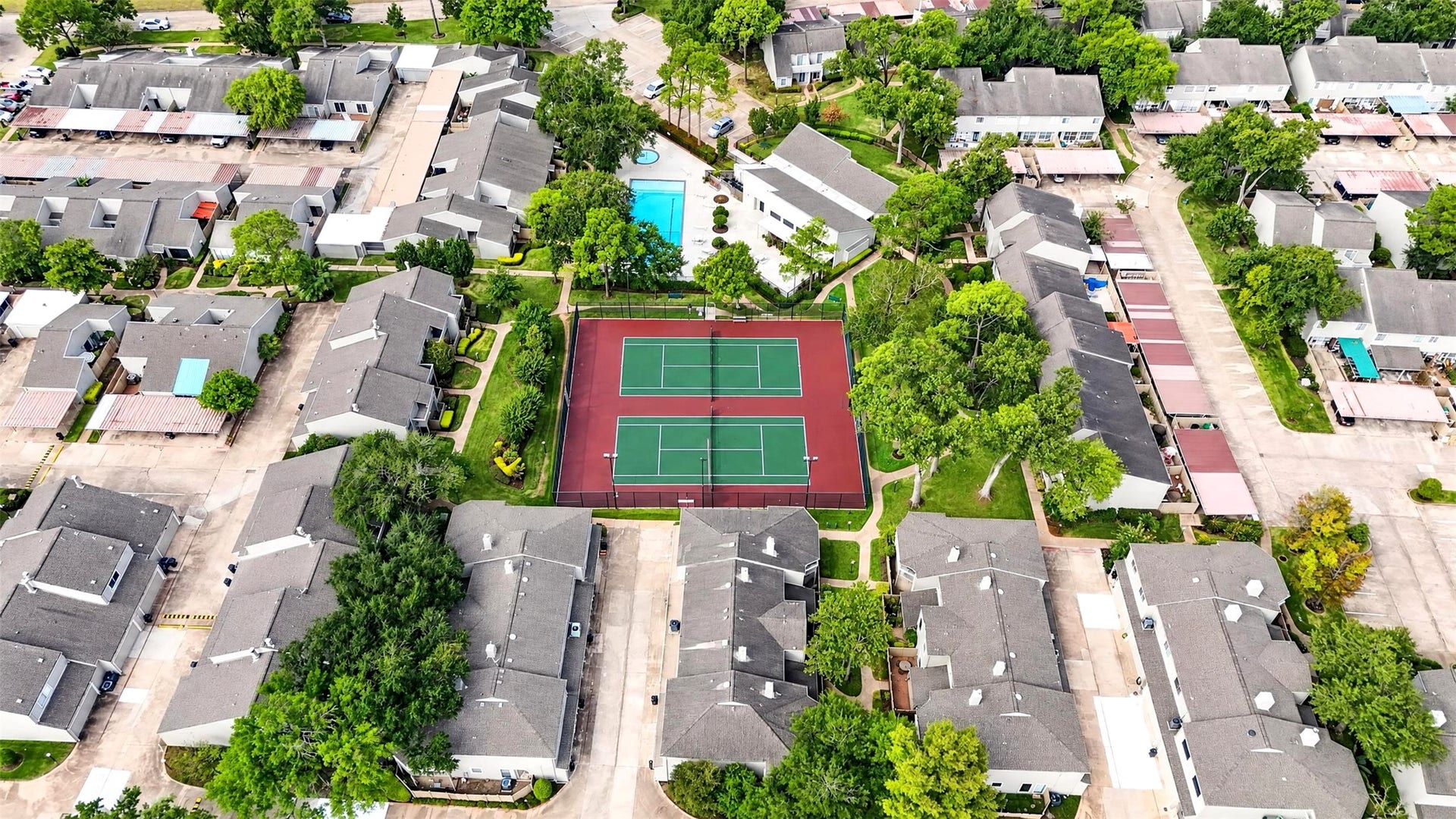 2379 Briarwest Boulevard, #85, Houston, TX 77077 Aerial view over the community's two tennis courts and pool, surrounded by townhome rooftops and mature trees.
