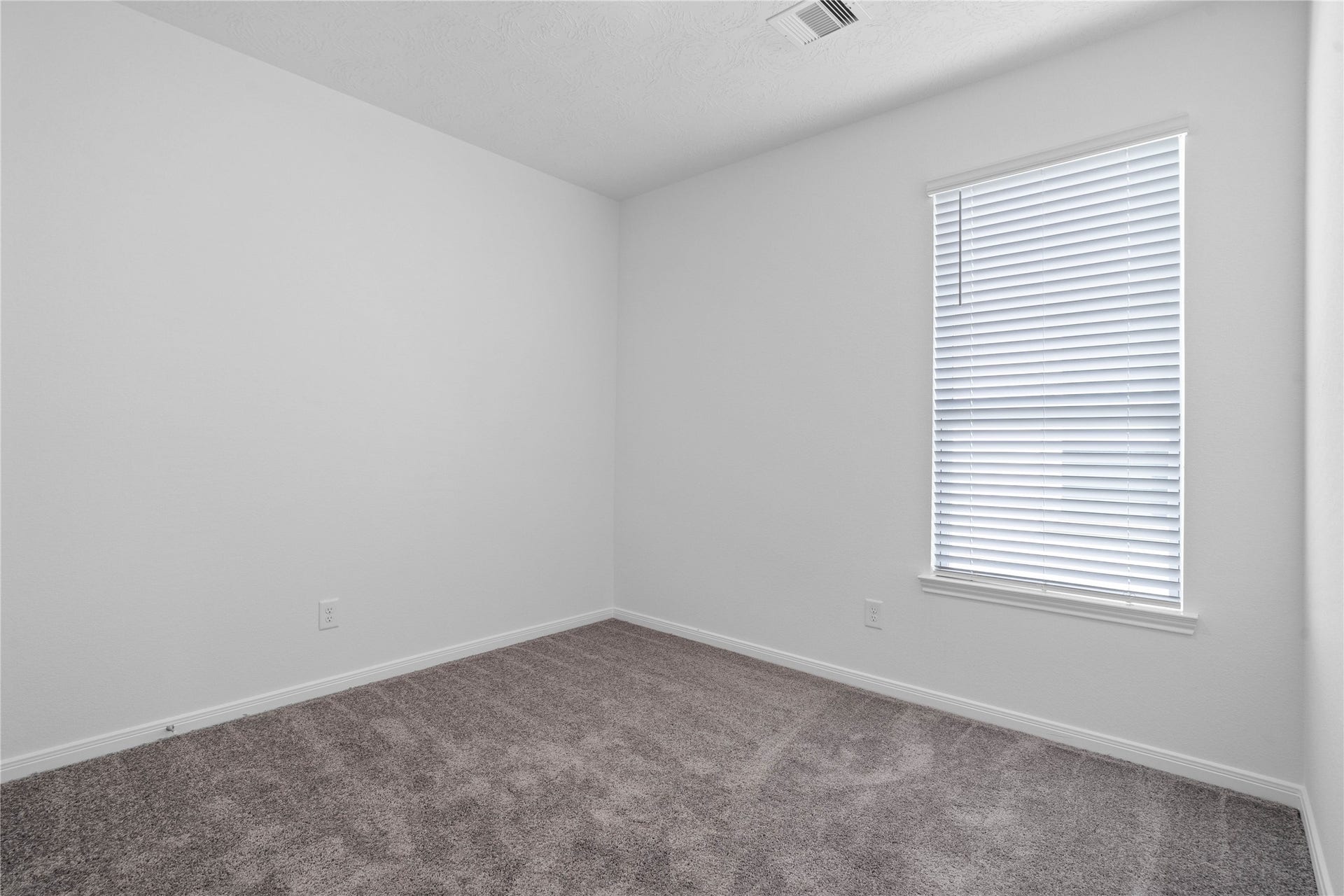 Light-filled secondary bedroom complete with cozy carpet flooring, ample closet space, and a large window fitted with blinds.