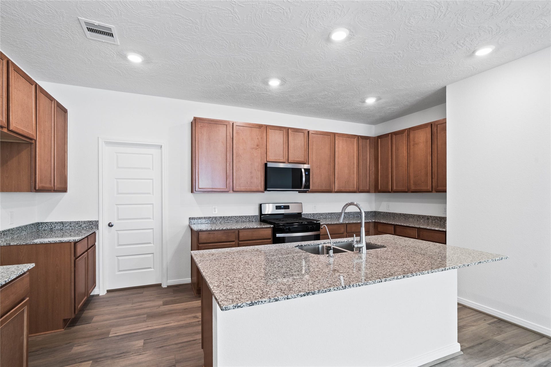 The central kitchen island features a durable granite countertop and an undermount stainless steel sink with a Moen faucet. The kitchen island has additional storage space, increased counter and prep space, and is the social hub of the home--where family and guests gather and interact!