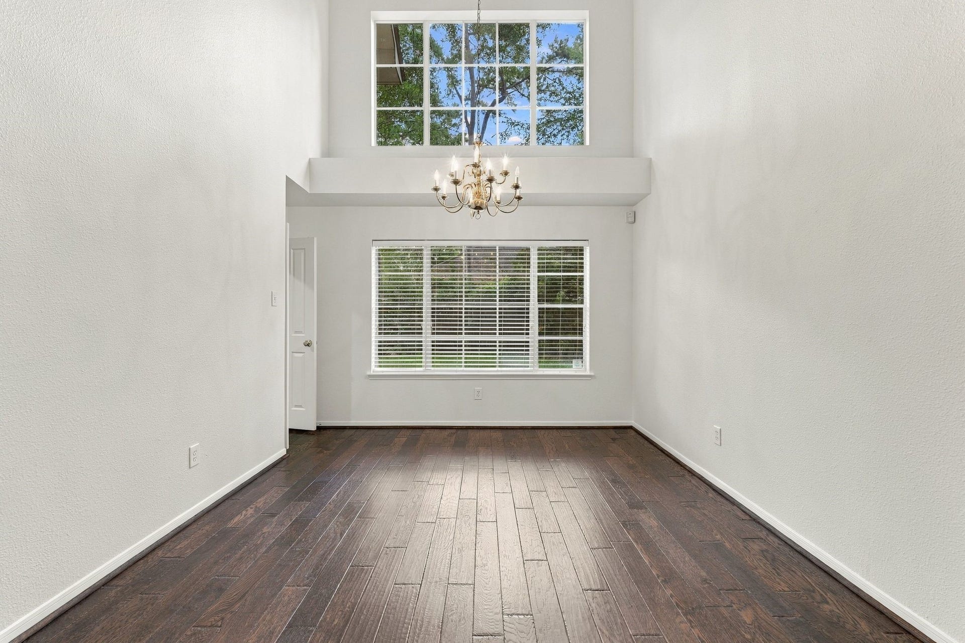 202 W Greywing Circle, The Woodlands, TX 77382 Bright and open living space with soaring ceilings, elegant dark hardwood floors, and abundant natural light from large windows, enhanced by a classic chandelier.