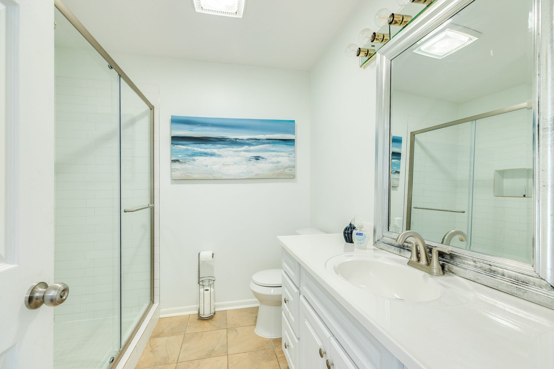 Bright bathroom features a spacious vanity with white cabinetry, framed mirror, brushed-nickel-style fixtures, and a glass-enclosed shower with white subway tile surround.
