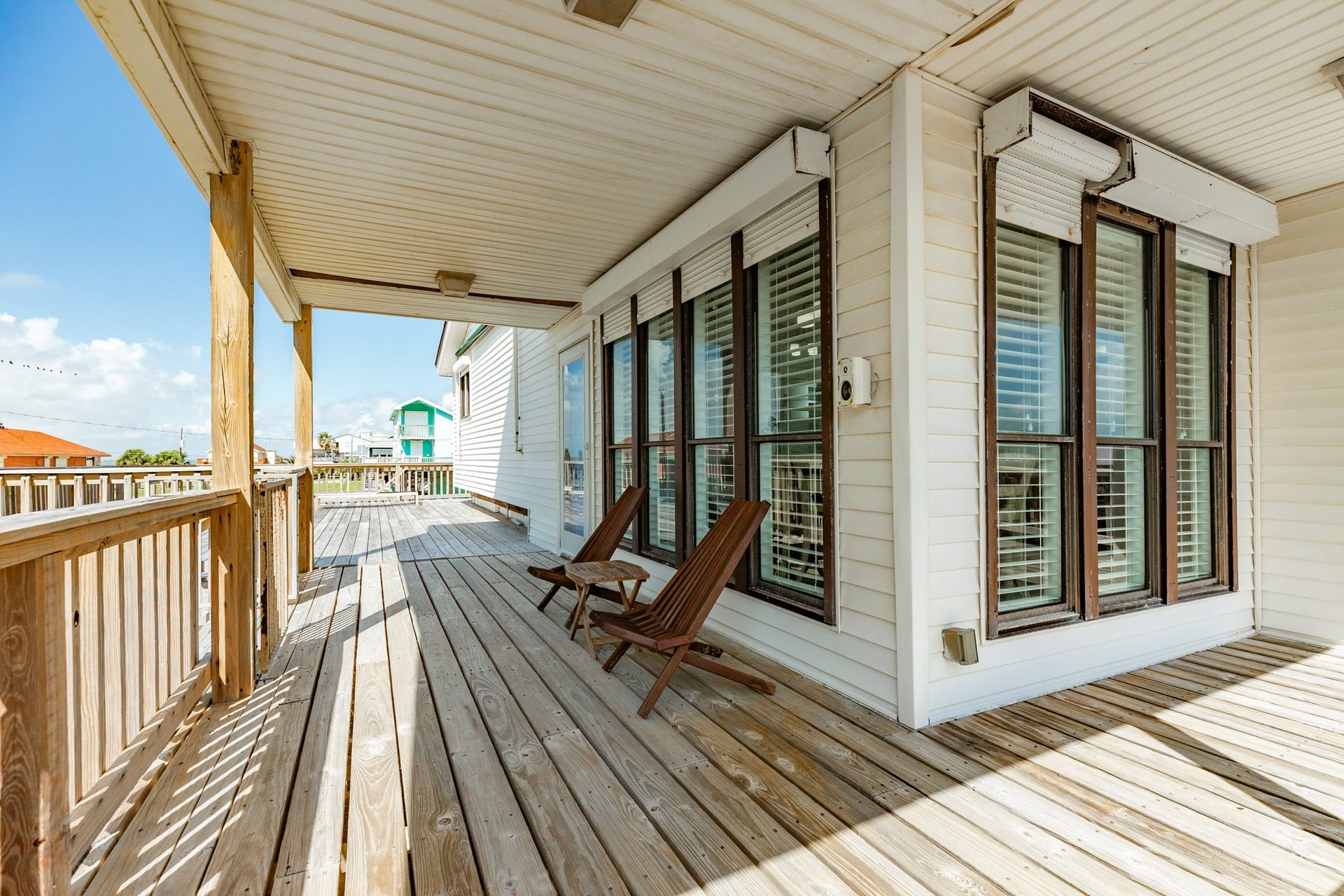 Welcoming covered porch features wooden decking, large windows, and a shaded seating area for relaxing while enjoying the coastal breeze.