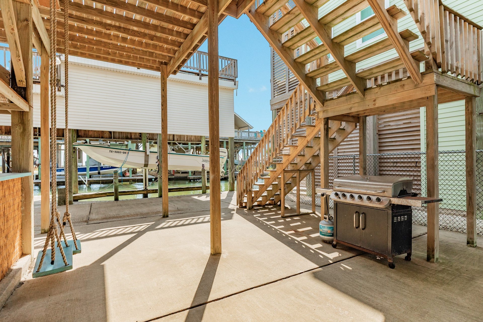 Generous ground-level patio features a grilling station, wooden stairway, and shaded gathering space beneath the elevated home.