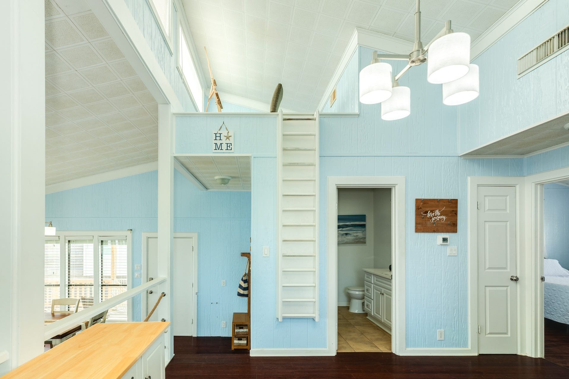 Vaulted ceilings enhance the airy kitchen, while a built-in ladder provides access to the upper loft area. Nearby doorways connect to the bedrooms and bathroom.