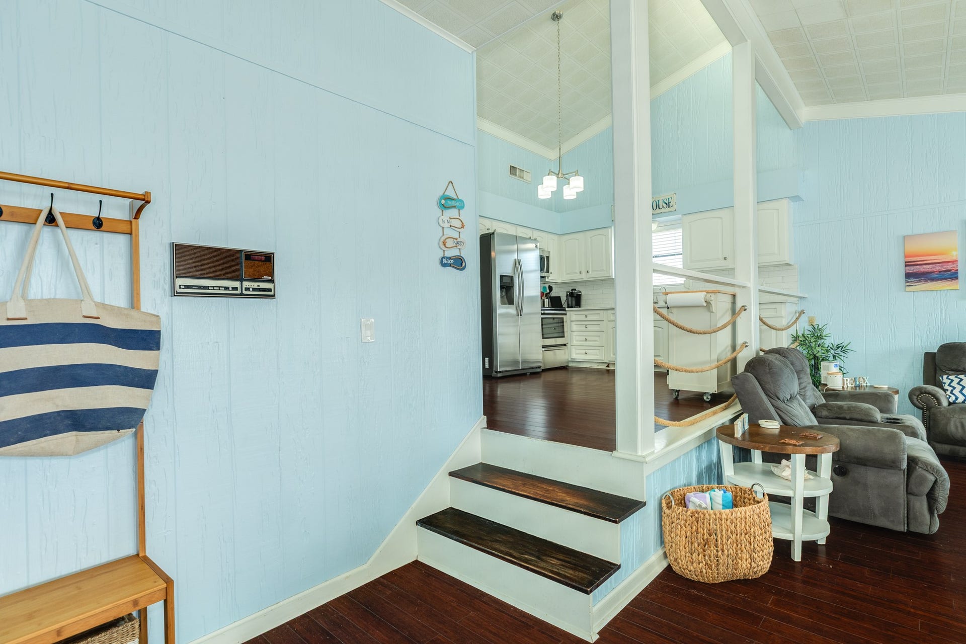 A short staircase leads from the living area to the elevated kitchen, with decorative rope railings, coastal-inspired finishes, and an open design that connects the spaces.