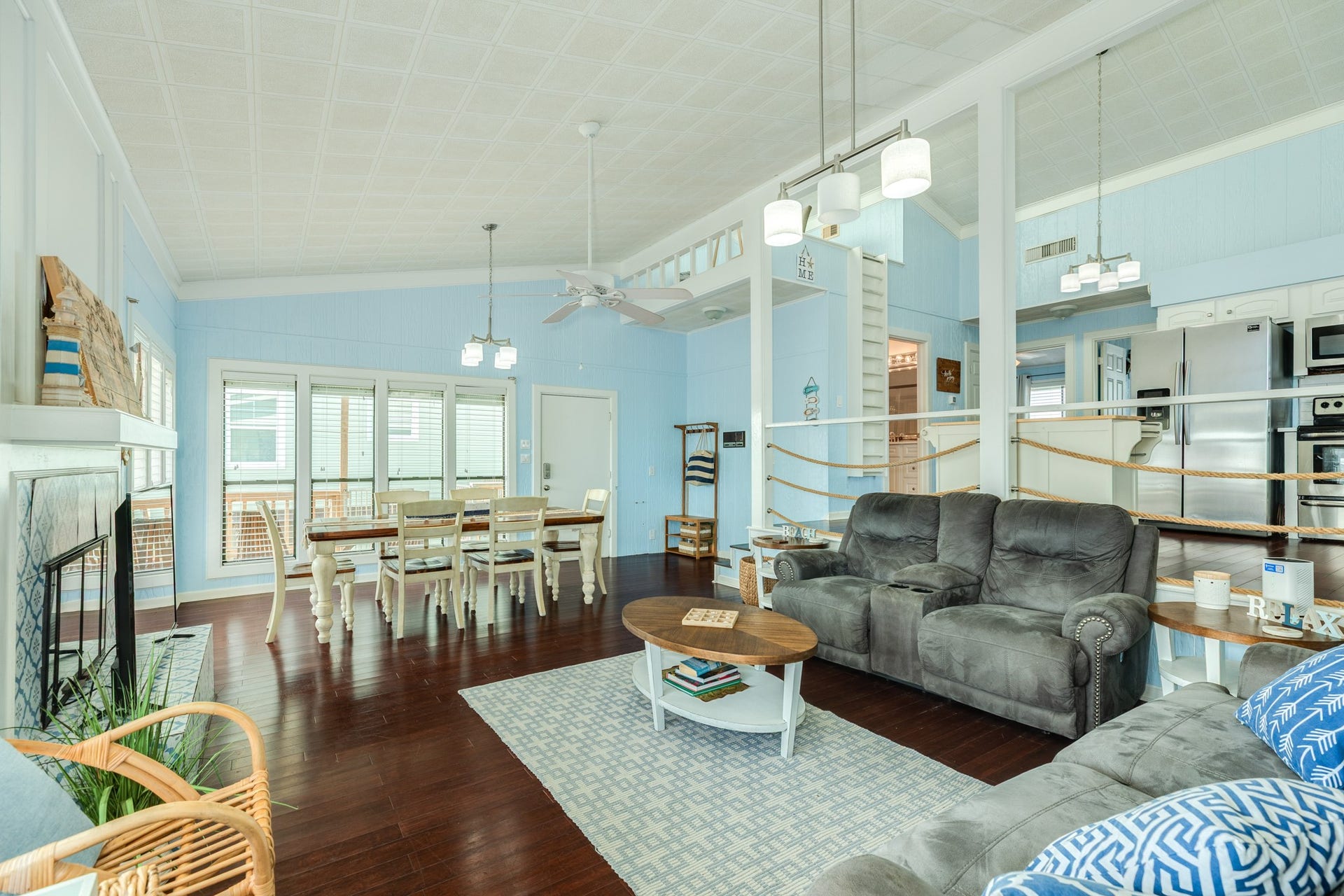 Spacious living and dining areas feature vaulted ceilings, rich wood-look flooring, coastal blue walls, and an open layout connecting the kitchen and gathering spaces.