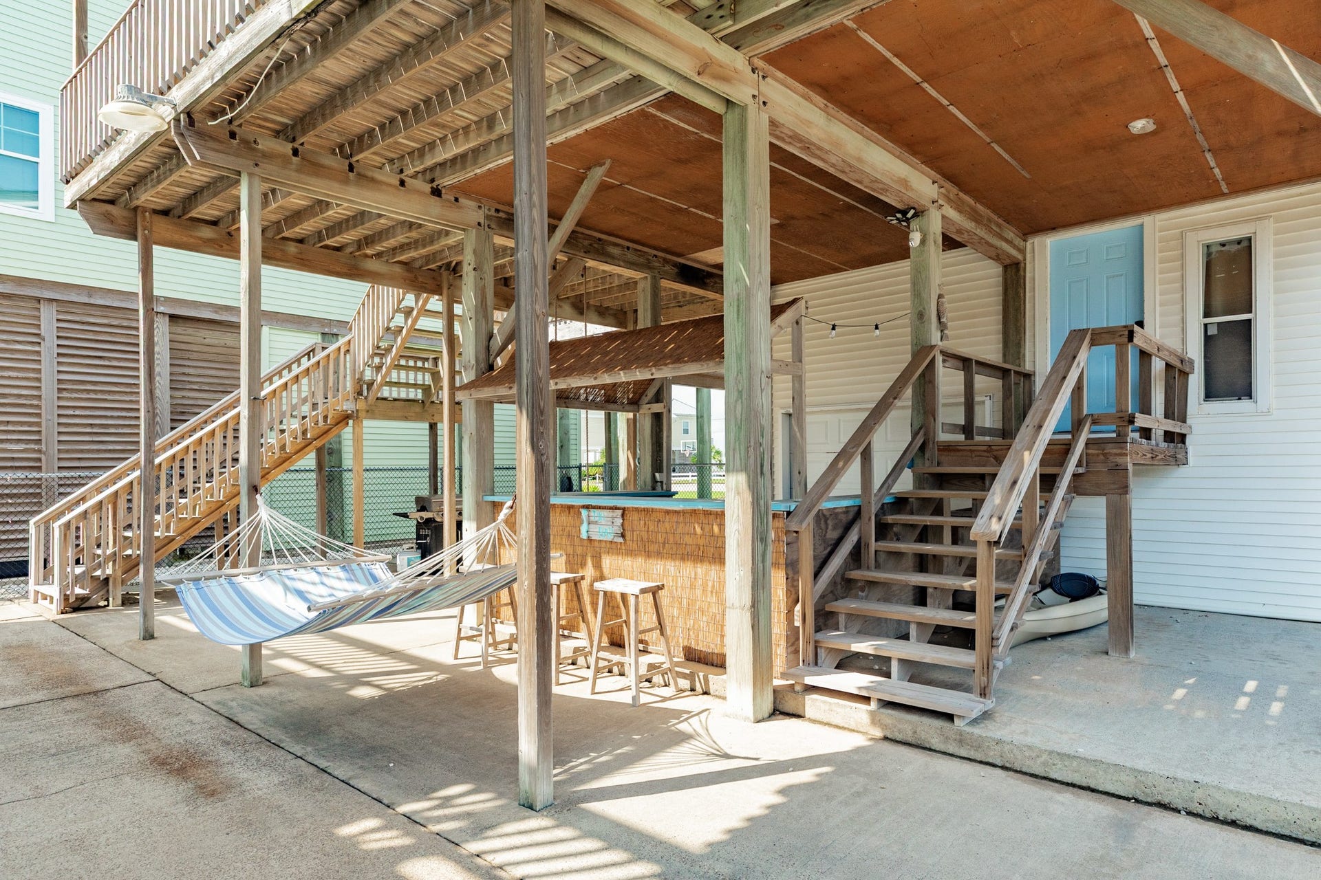 Spacious covered area beneath the home features a concrete patio, hammock, tiki-style bar, and convenient stairway access to the upper decks.