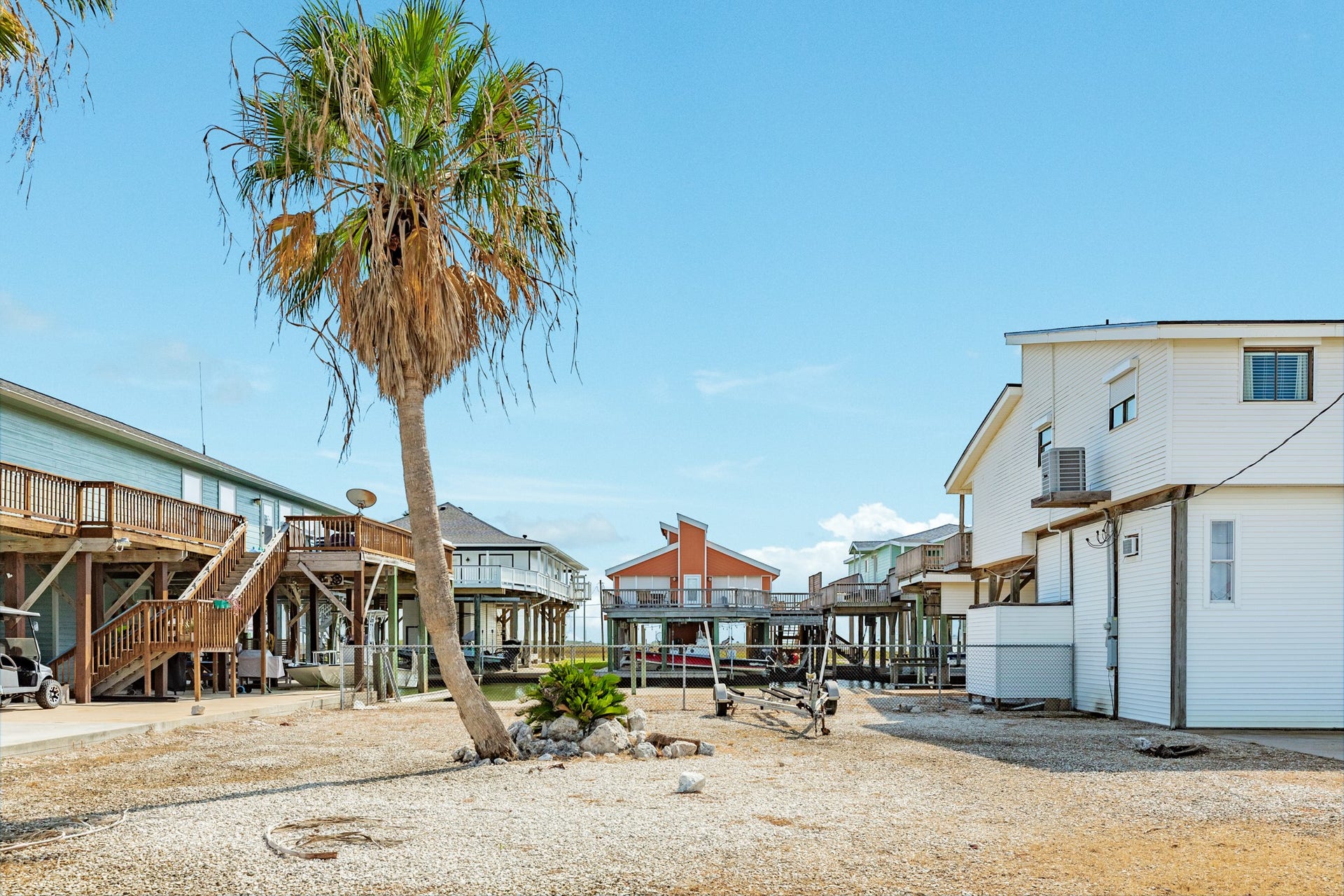 Generous gravel-covered yard offers flexible outdoor space, accented by a mature palm tree and convenient access to the home's garage and driveway.