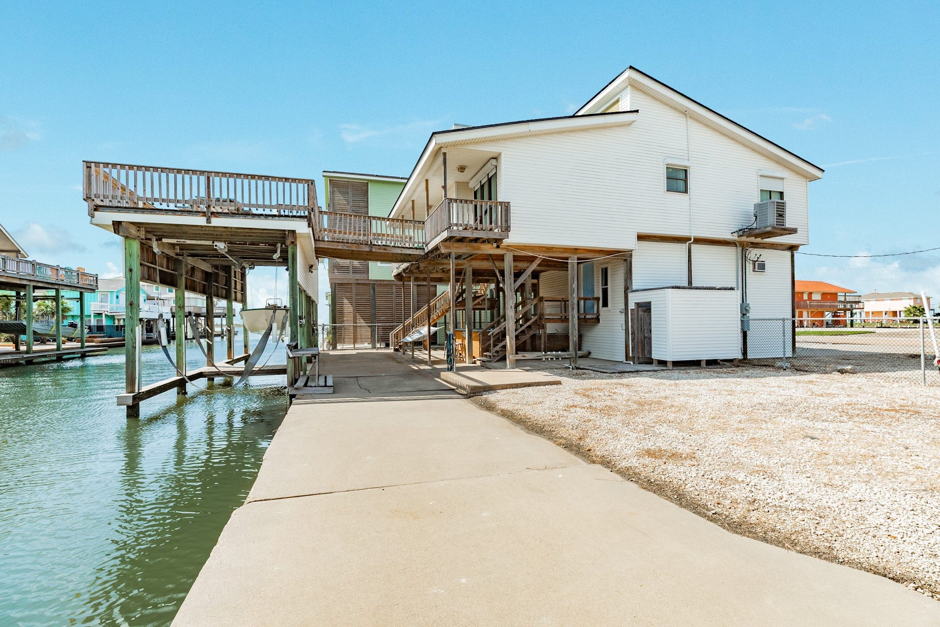 Waterfront exterior showcases the elevated home, covered boat lift, concrete bulkhead, and multiple decks overlooking the canal.