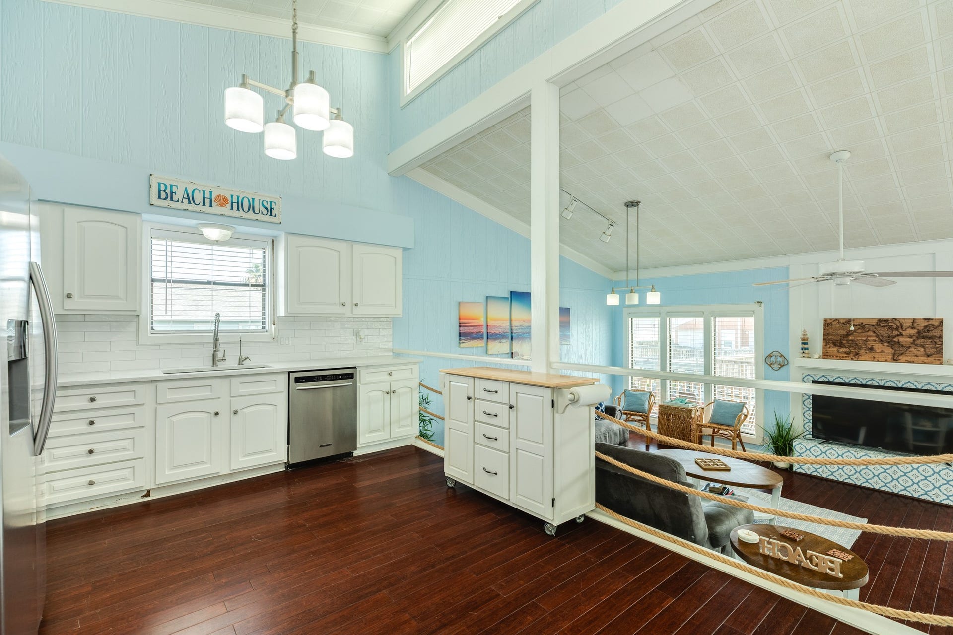 Elevated kitchen offers an open view into the living room, featuring white cabinetry, a movable island with butcher-block top, and decorative rope railings that complement the coastal design.