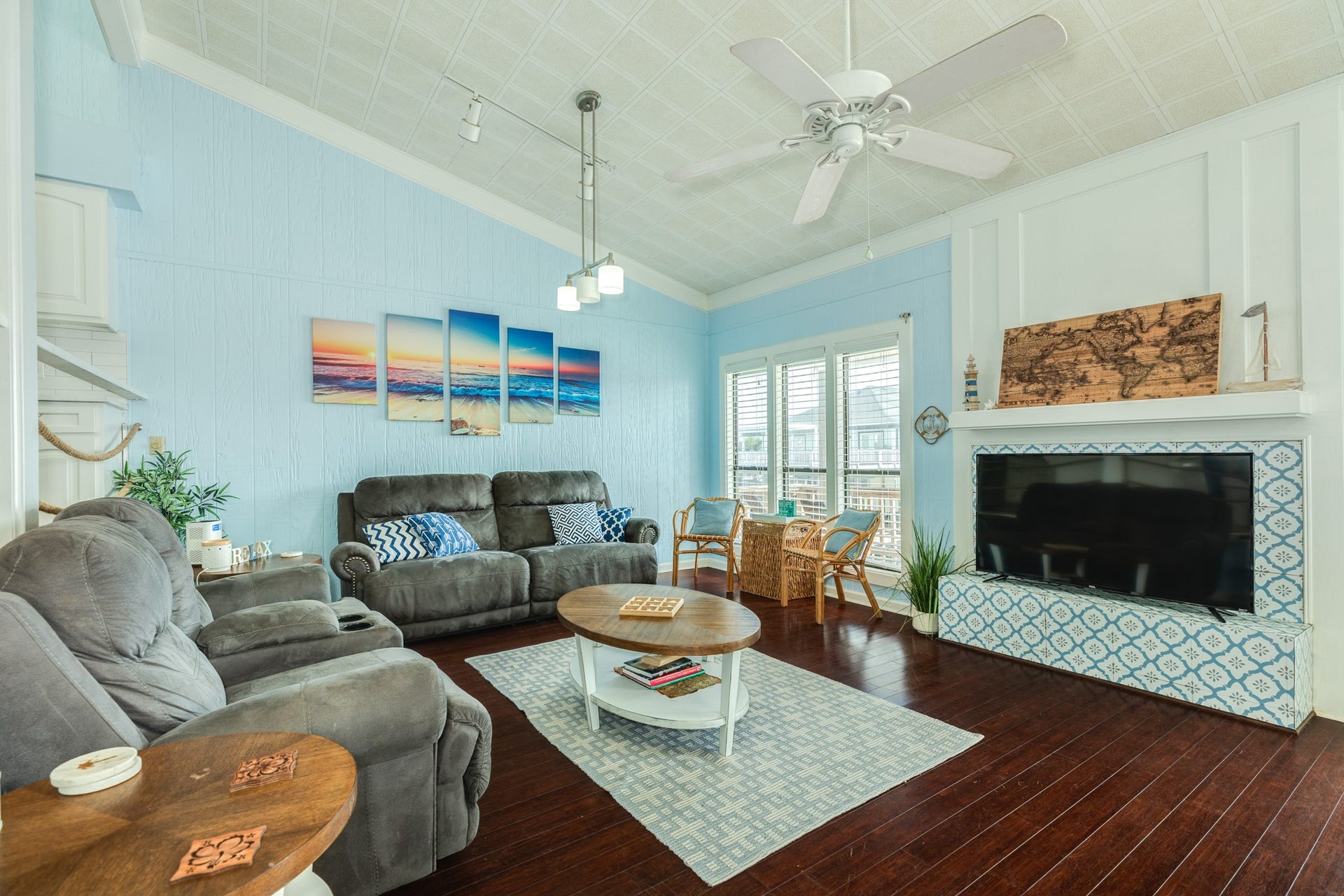Inviting living room features vaulted ceilings, a ceiling fan, comfortable seating, and a decorative blue-and-white tiled fireplace surround that serves as a charming focal point.