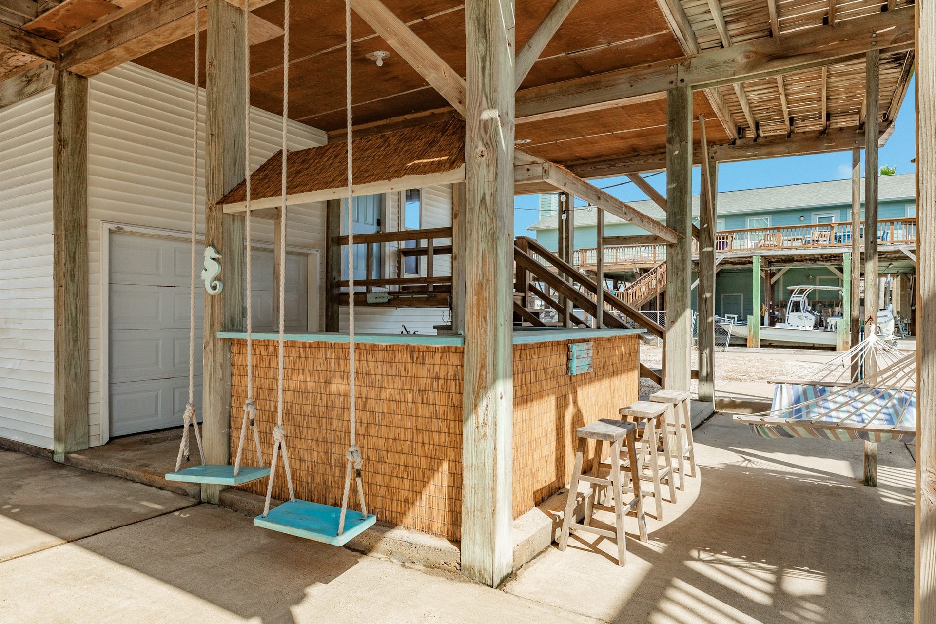 Coastal-inspired tiki bar features bamboo-style accents, countertop seating, wooden barstools, and hanging swings, creating a fun setting for outdoor entertaining.