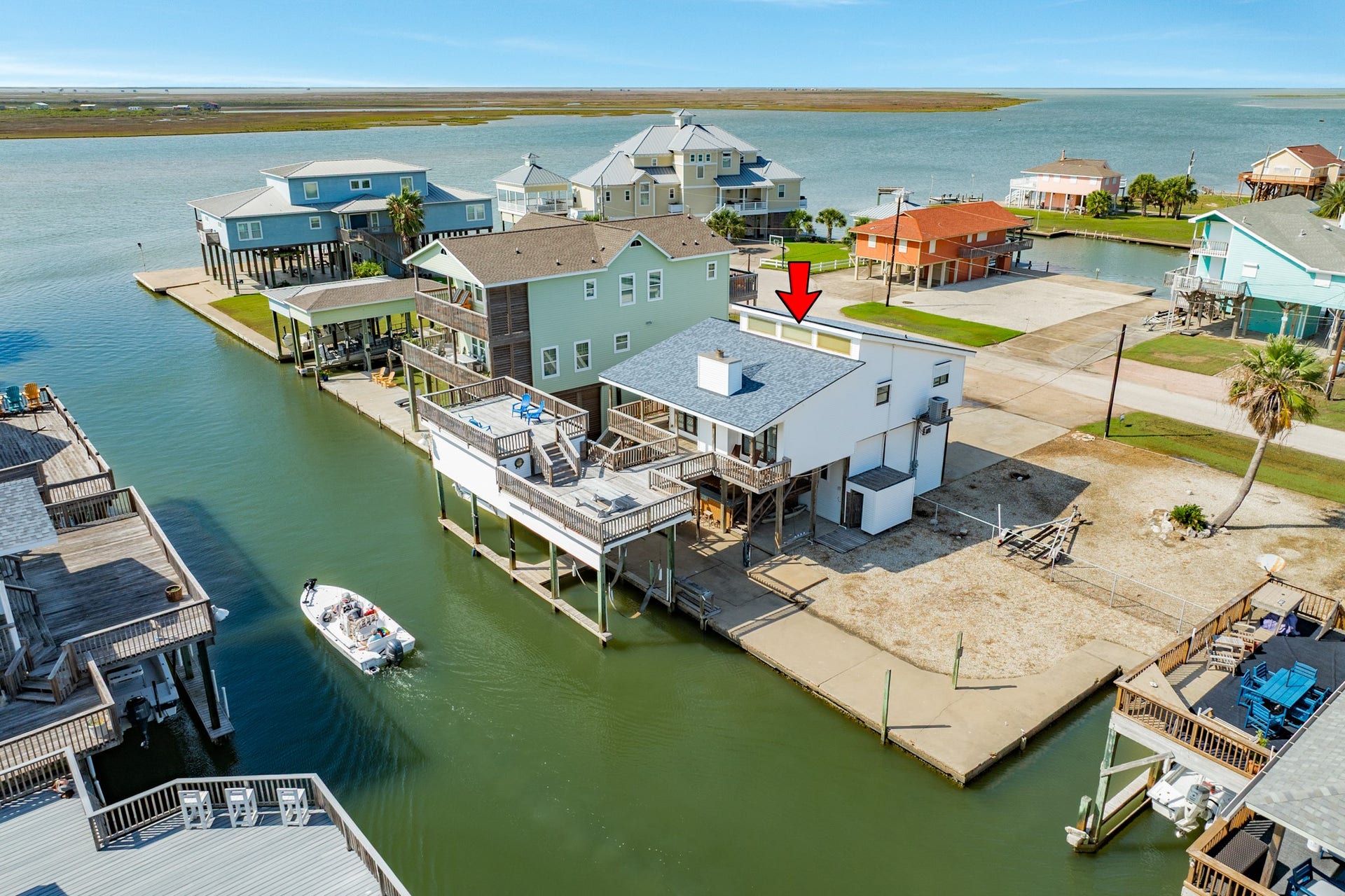 Elevated view highlights the home's canal frontage, multiple outdoor decks, and generous yard space, with open bay waters just beyond the neighborhood.