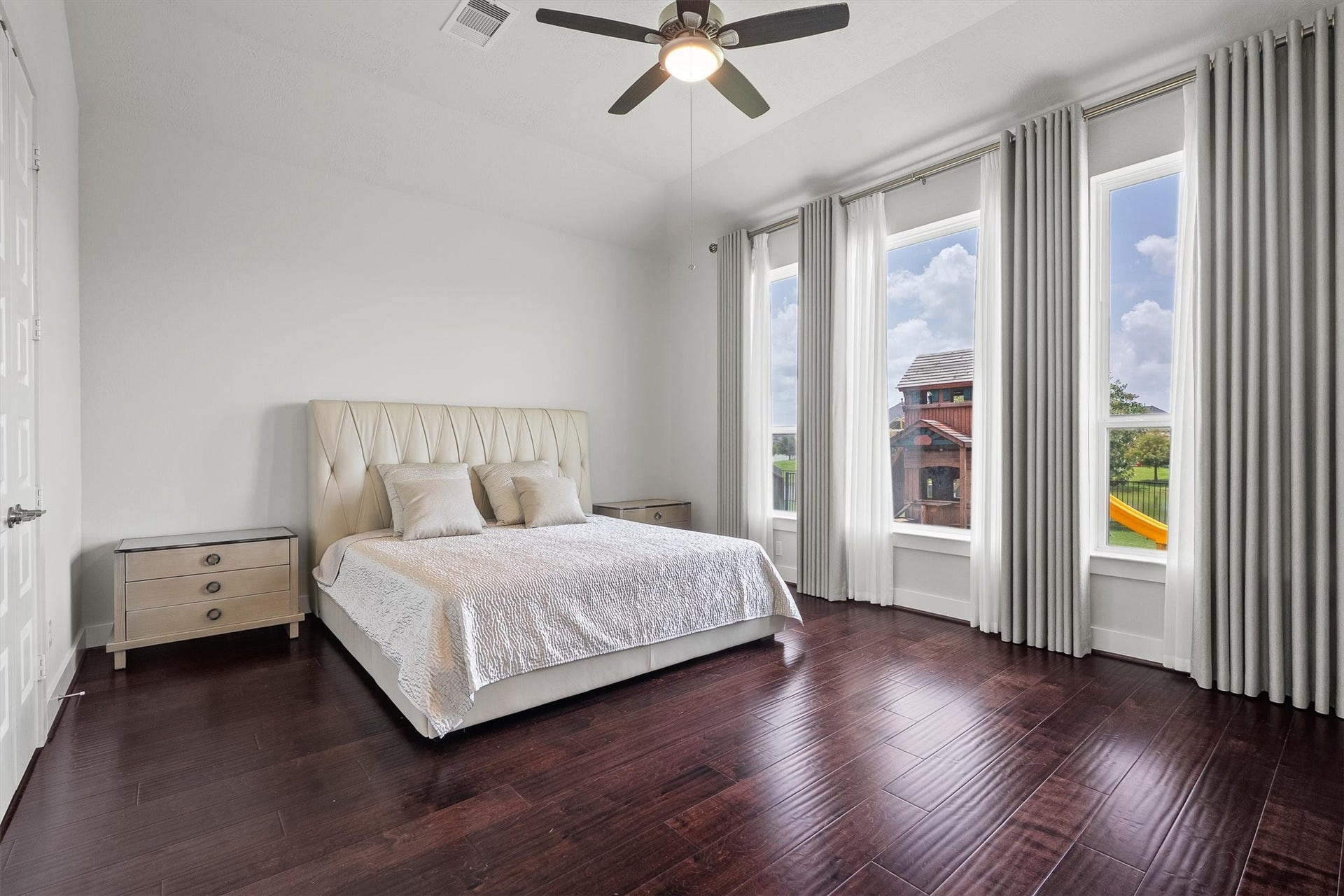 Escape to the spacious primary suite, hard wood floor, highlighted by large sun filled windows, a stylish modern wood ceiling fan, and rich wood flooring, offering a peaceful and comfortable retreat to unwind and recharge.