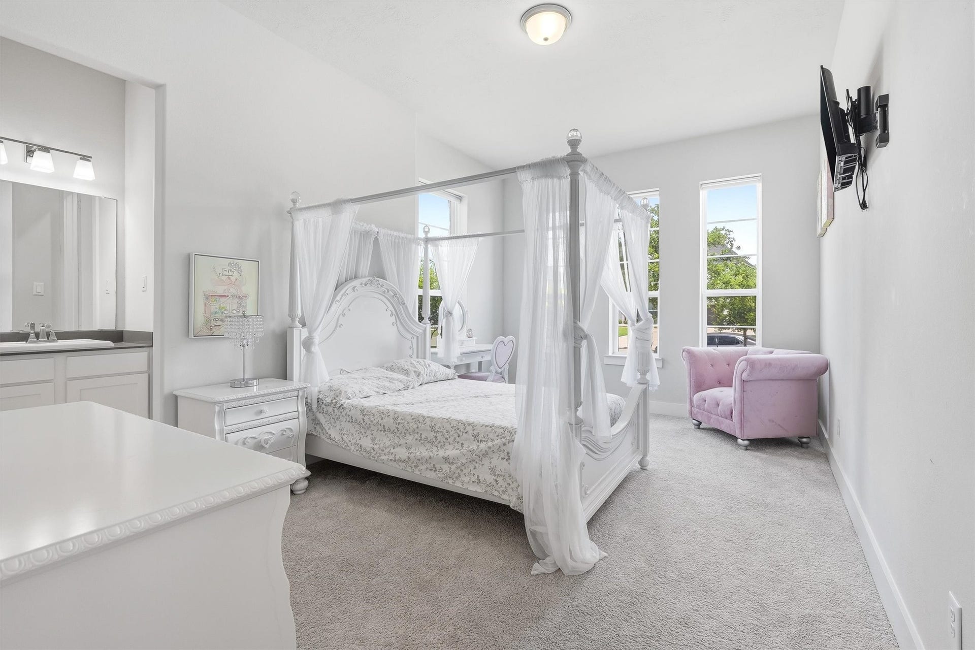 This inviting bedroom features plush carpeting, multiple sun-filled windows, and a private sink vanity with convenient access to a shared bathroom, creating a comfortable and functional space with added privacy.