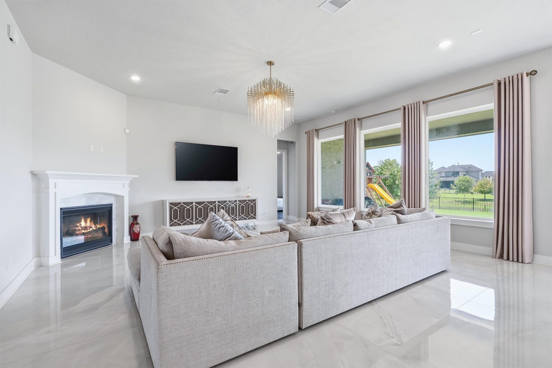 Make a statement in this breathtaking living room with soaring ultra-high ceilings, a wall of sun-filled windows, a striking fireplace, and gleaming tile flooringa stunning space that blends elegance, comfort, and architectural drama.