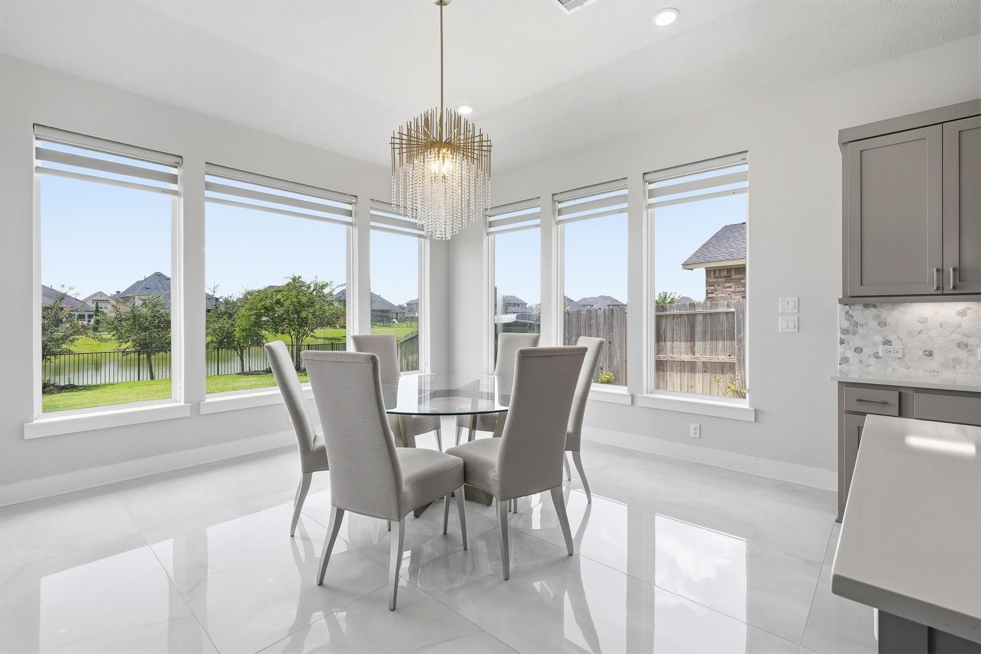 Enjoy a bright and inviting breakfast area complete with a beautiful modern chandelier, sleek tile flooring, and multiple windows that fill the space with natural light and create a warm, inviting atmosphere for every meal.