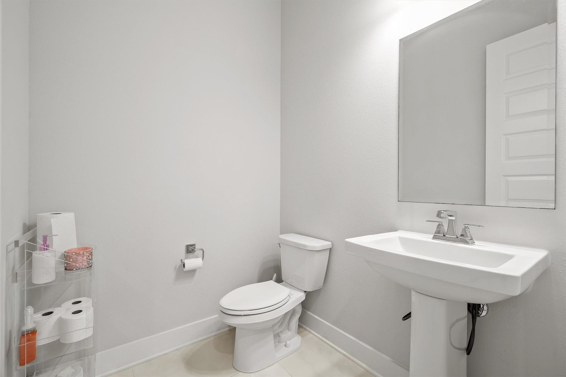 The guest bathroom features a sleek pedestal sink and a modern toilet  combining simplicity and elegance for a welcoming space.