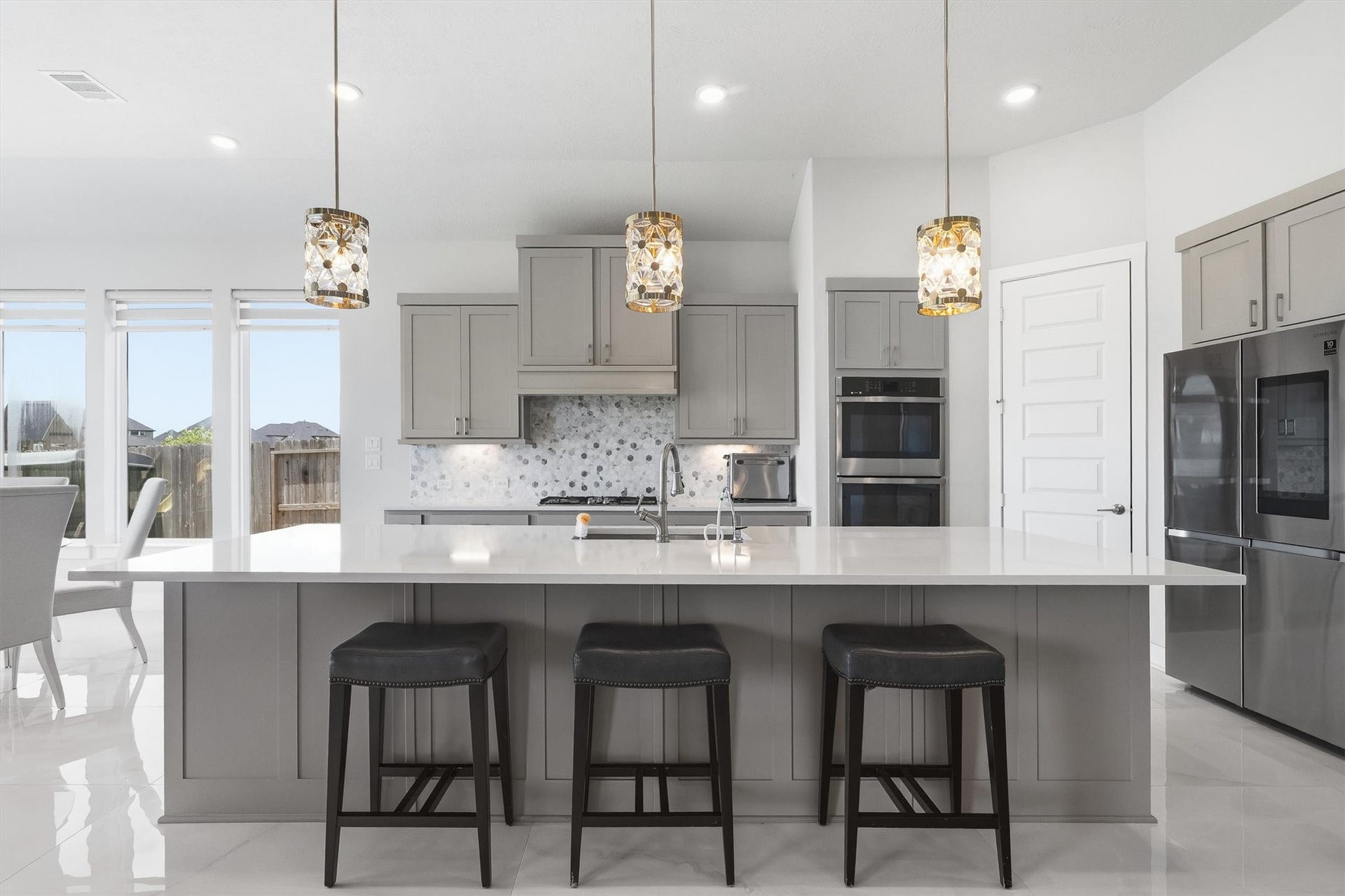 Step into this beautifully designed kitchen featuring gleaming quartz countertops, a large center island, modern grey cabinetry, and modern pendant lighting, an ideal setting for cooking, gathering, and entertaining.