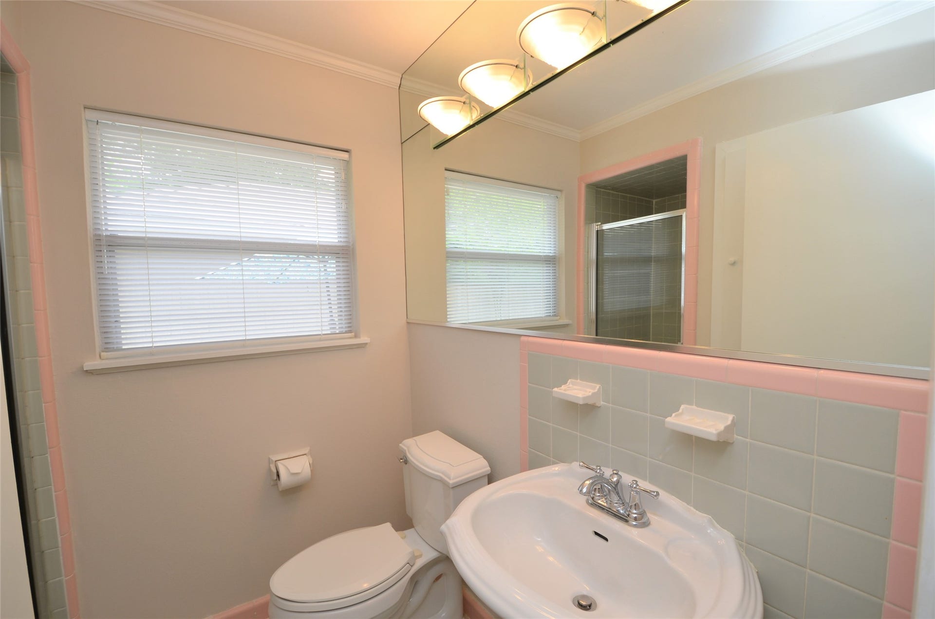 Bright master bathroom with enclosed shower featuring stylish Hollywood lighting and an expansive mirror for a touch of glamour.