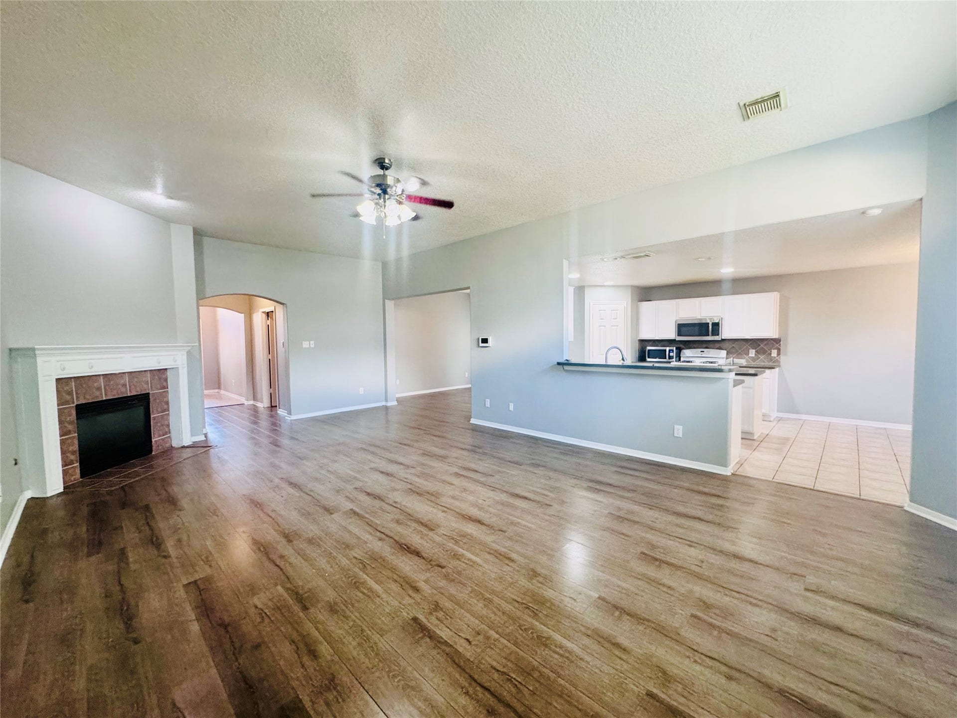Spacious open-concept living area with elegant wood flooring, a cozy fireplace, and a modern kitchen featuring stainless steel appliances and a convenient bar counter for casual dining.