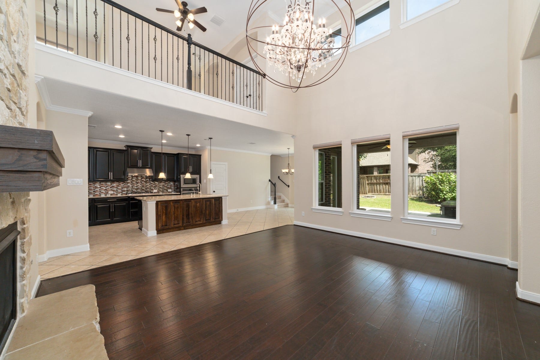 17302 Milrig Court, Richmond, TX 77407 Stunning open-concept living area features soaring ceilings, elegant chandelier, and abundant natural light from large windows, seamlessly connecting to a modern kitchen with dark cabinetry and a stylish island.