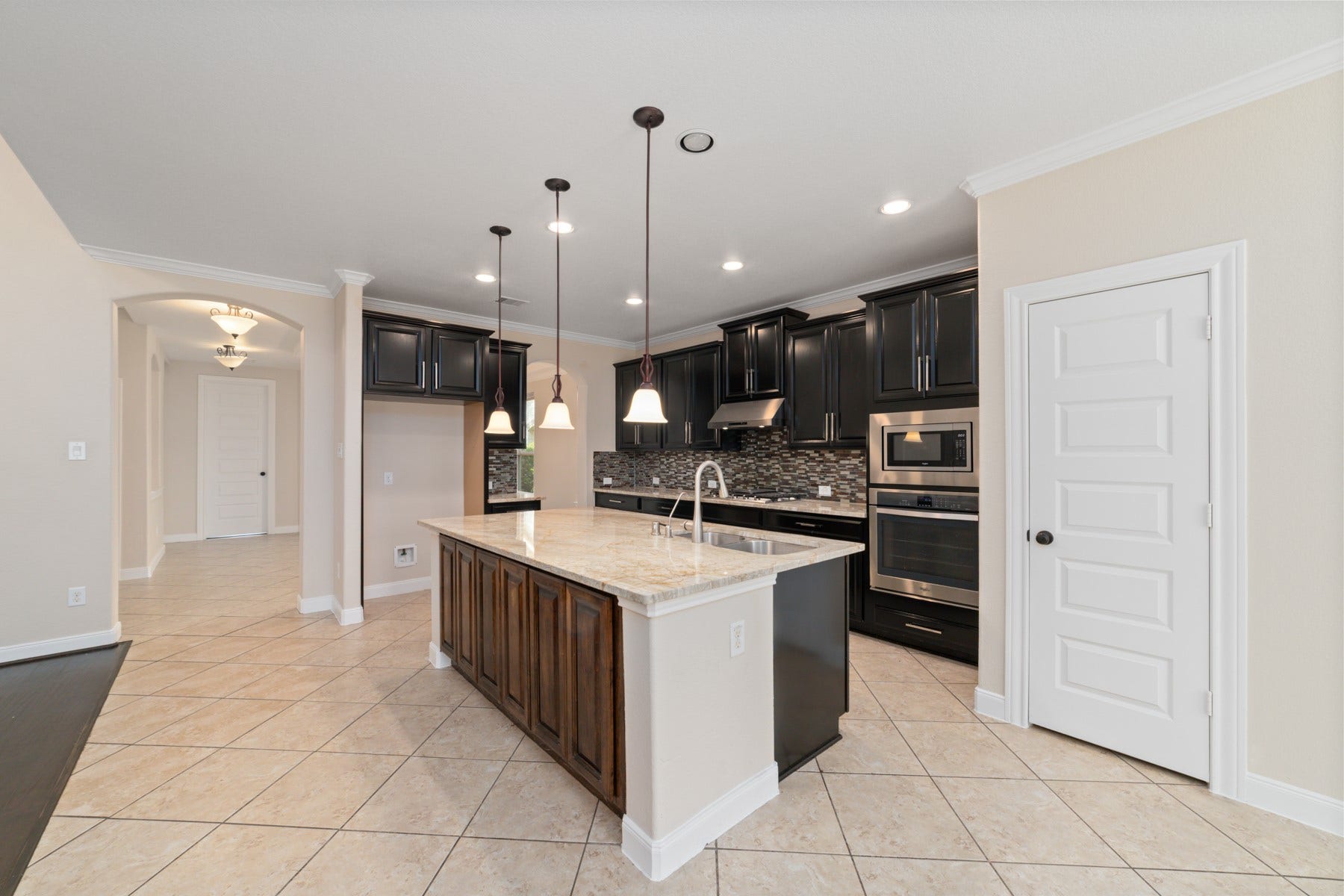 17302 Milrig Court, Richmond, TX 77407 Elegant kitchen featuring dark cabinetry, a large center island with granite countertops, and modern stainless steel appliances, all under stylish pendant lighting.