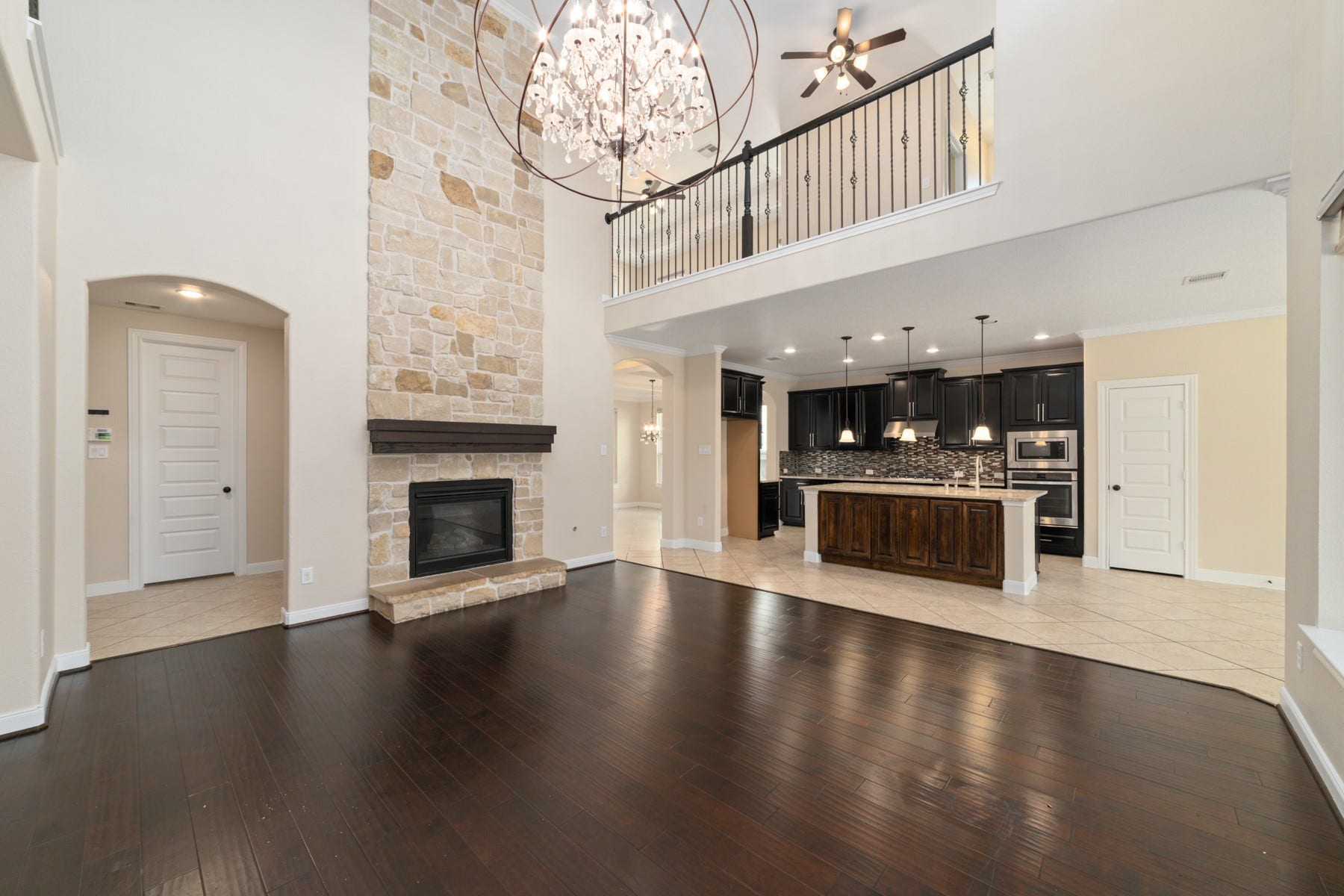 17302 Milrig Court, Richmond, TX 77407 Stunning living space with a dramatic stone fireplace, elegant chandelier, and open concept layout leading to a modern kitchen with dark cabinetry and an island.